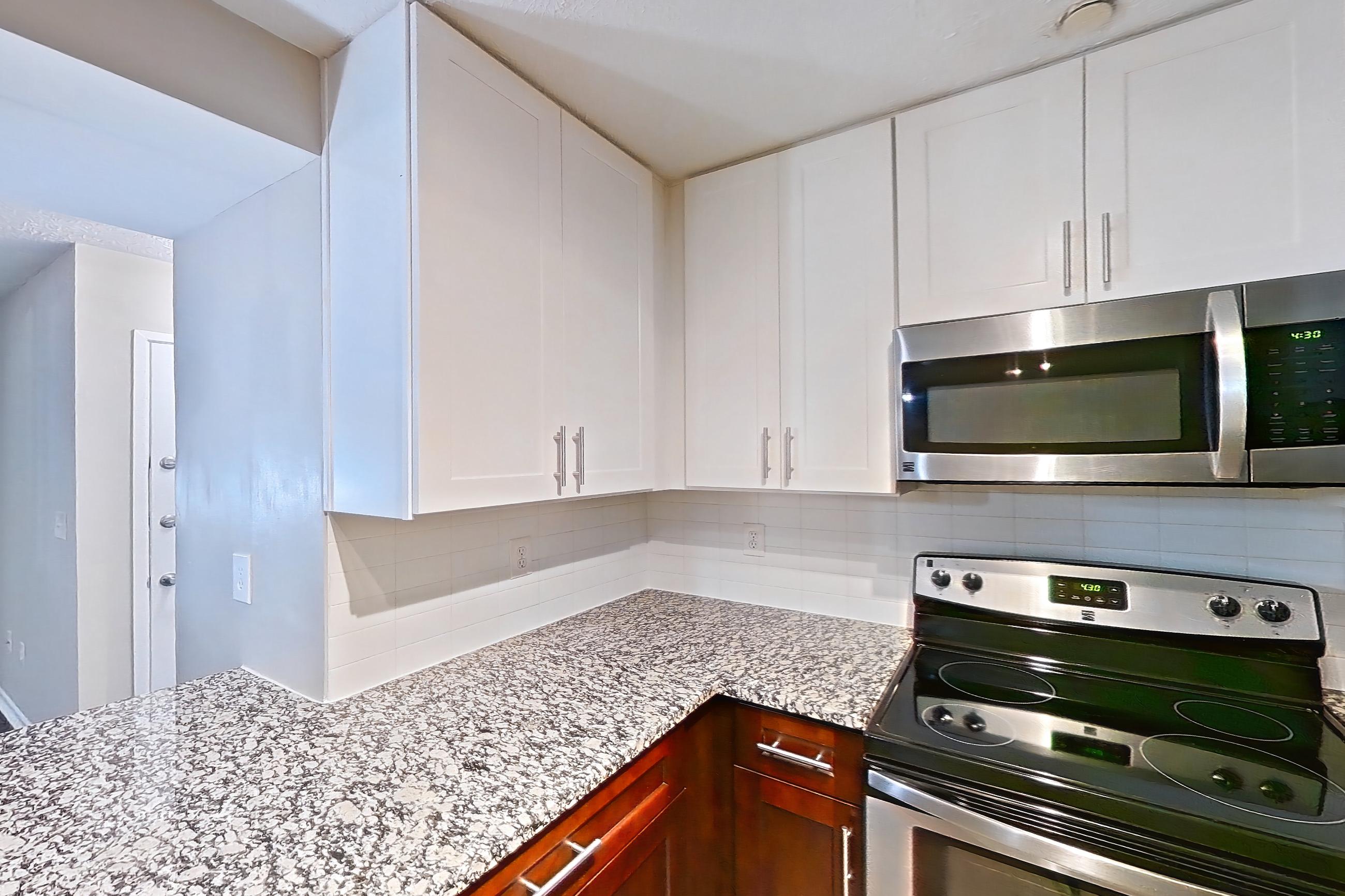 Kitchen with dark wood-finish flooring, dishwasher, electric range, light countertops, light stone countertops, light wood-finish flooring, microwave, oven/range, refrigerator, and stainless steel appliances, Apartment 2161D at Cortland at the Village