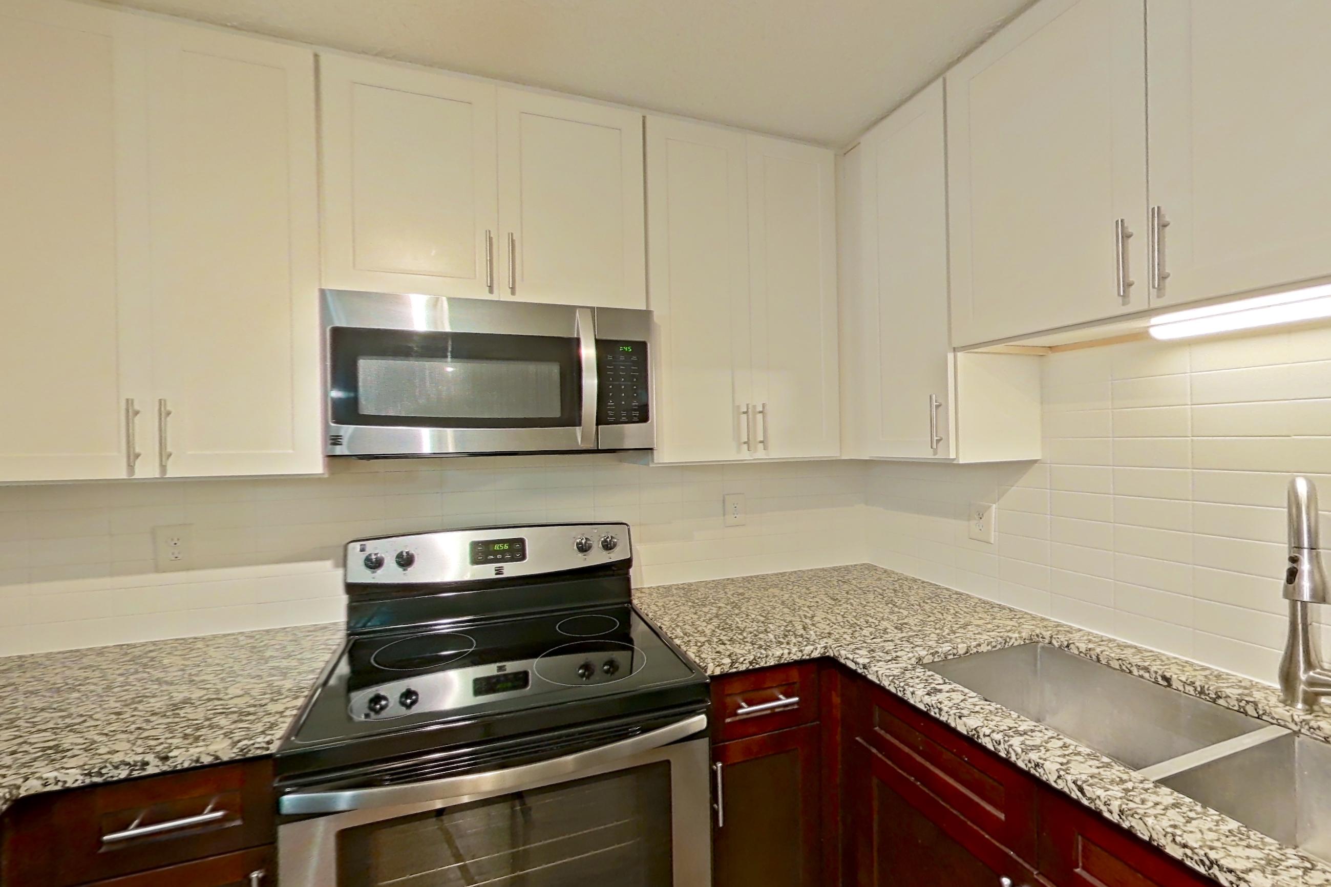 Kitchen with dishwasher, electric range, light countertops, light stone countertops, light wood-finish flooring, microwave, oven/range, refrigerator, and stainless steel appliances, Apartment 2163L at Cortland at the Village
