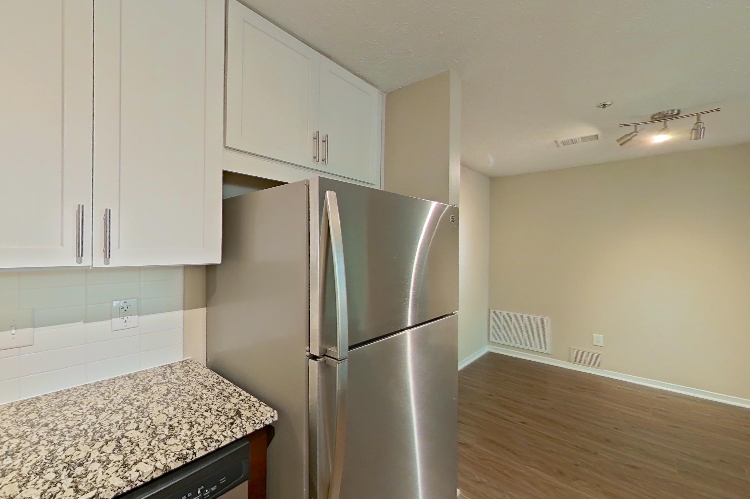 Kitchen with dishwasher, electric range, light countertops, light stone countertops, light wood-finish flooring, microwave, oven/range, refrigerator, and stainless steel appliances, Apartment 2163L at Cortland at the Village