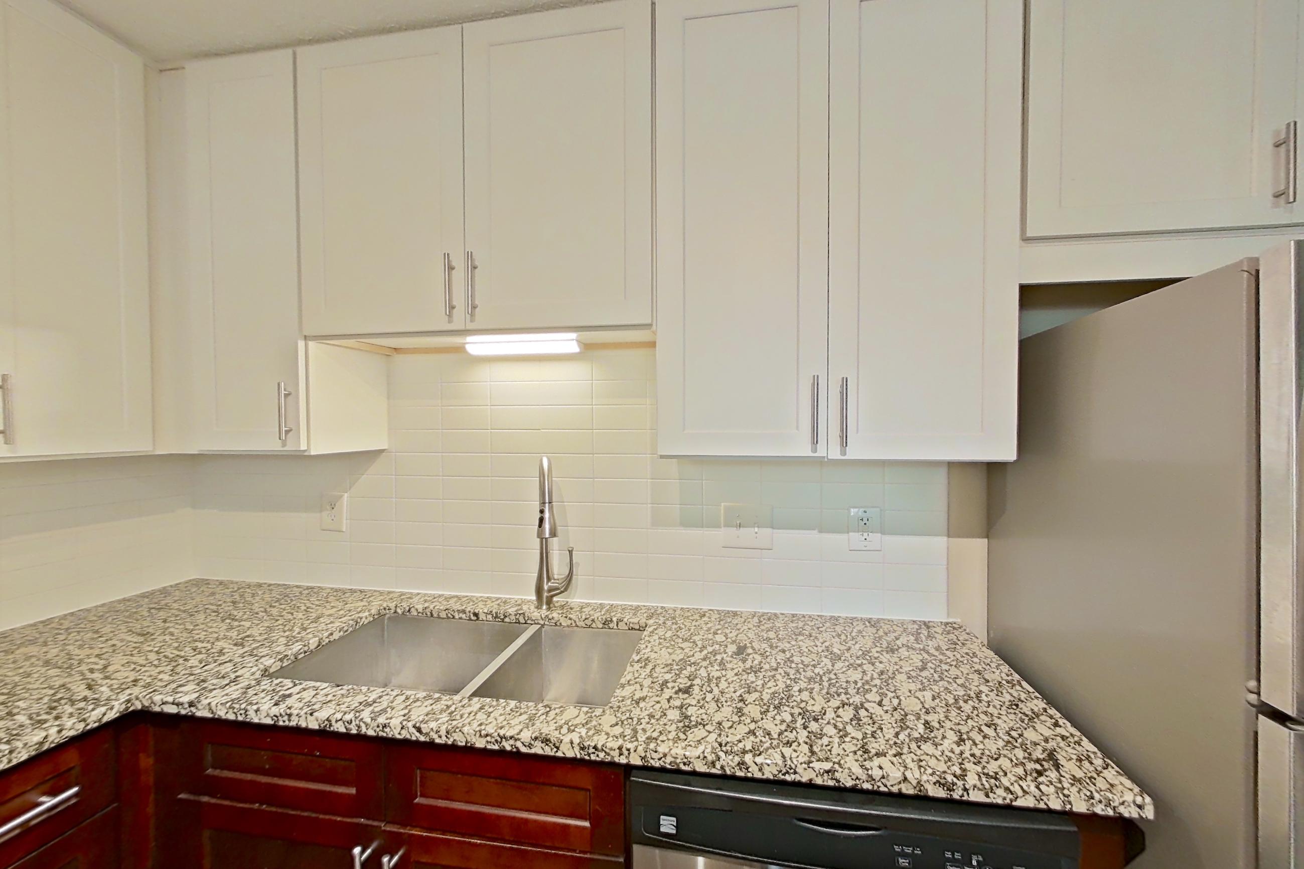 Kitchen with dishwasher, electric range, light countertops, light stone countertops, light wood-finish flooring, microwave, oven/range, refrigerator, and stainless steel appliances, Apartment 2163L at Cortland at the Village