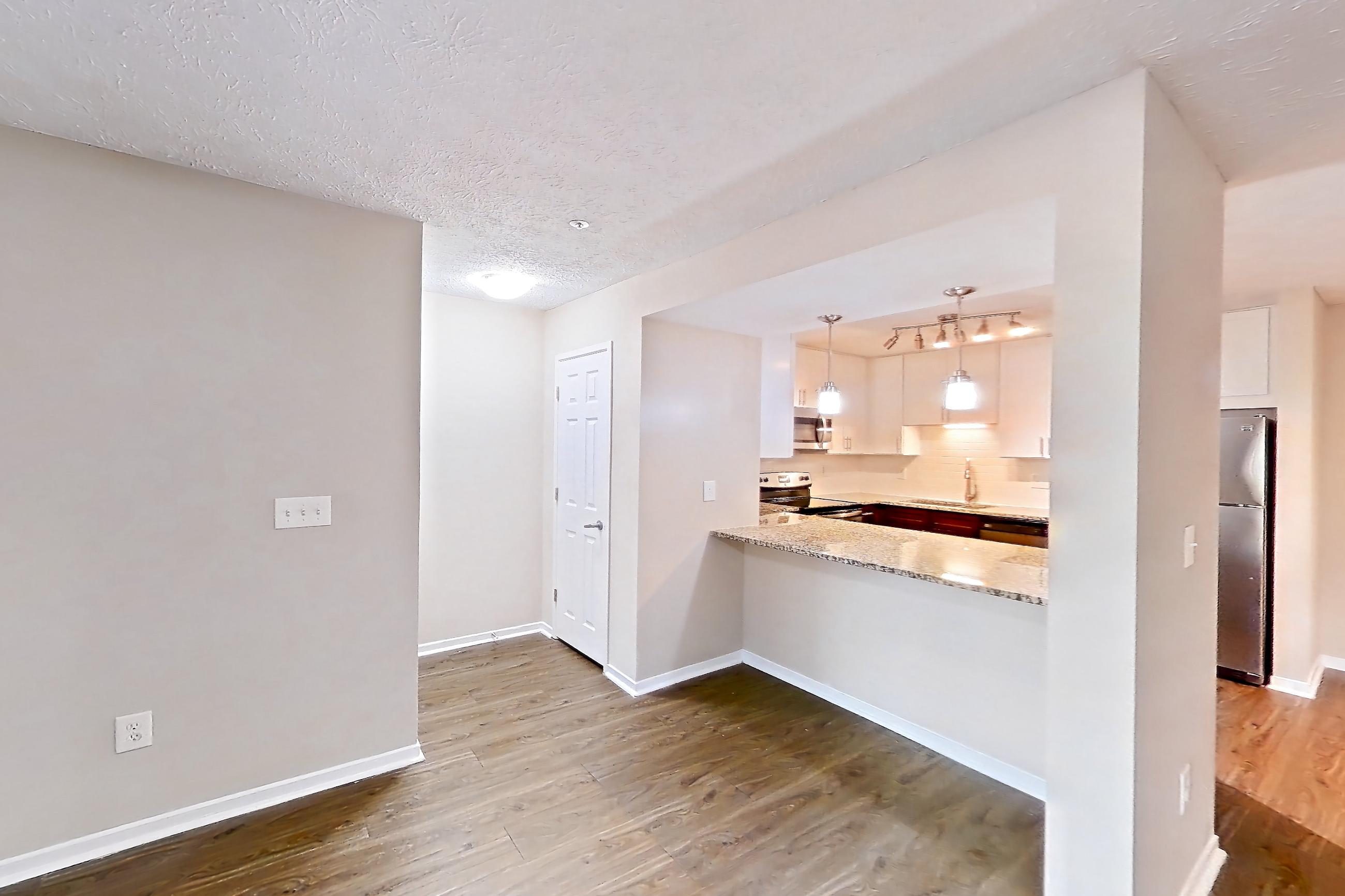 Living room with dark wood-finish flooring, dishwasher, electric range, light stone countertops, oven/range, refrigerator, and stainless steel appliances, Apartment 2163L at Cortland at the Village
