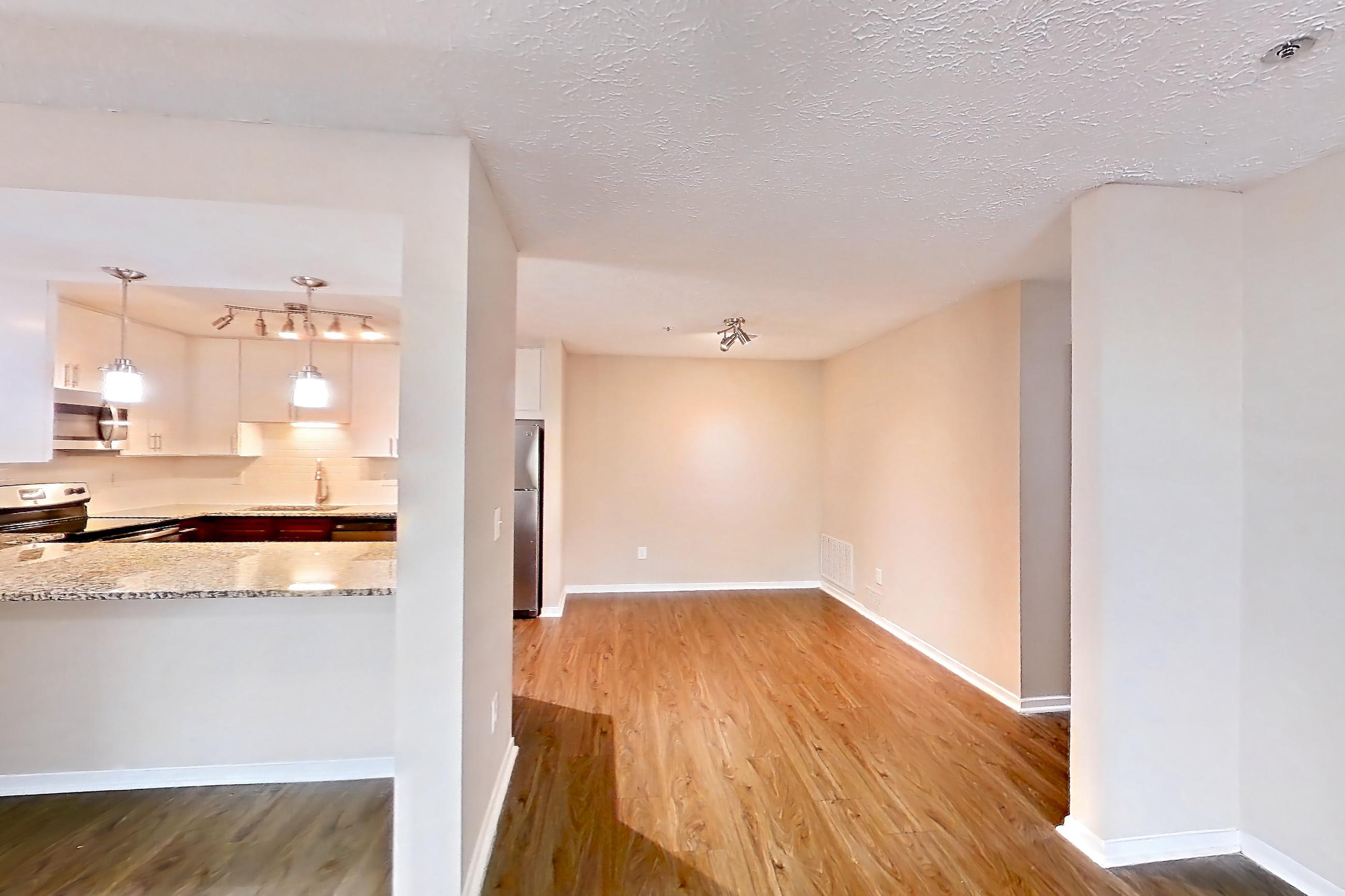 Living room with dark wood-finish flooring, dishwasher, electric range, light stone countertops, oven/range, refrigerator, and stainless steel appliances, Apartment 2163L at Cortland at the Village