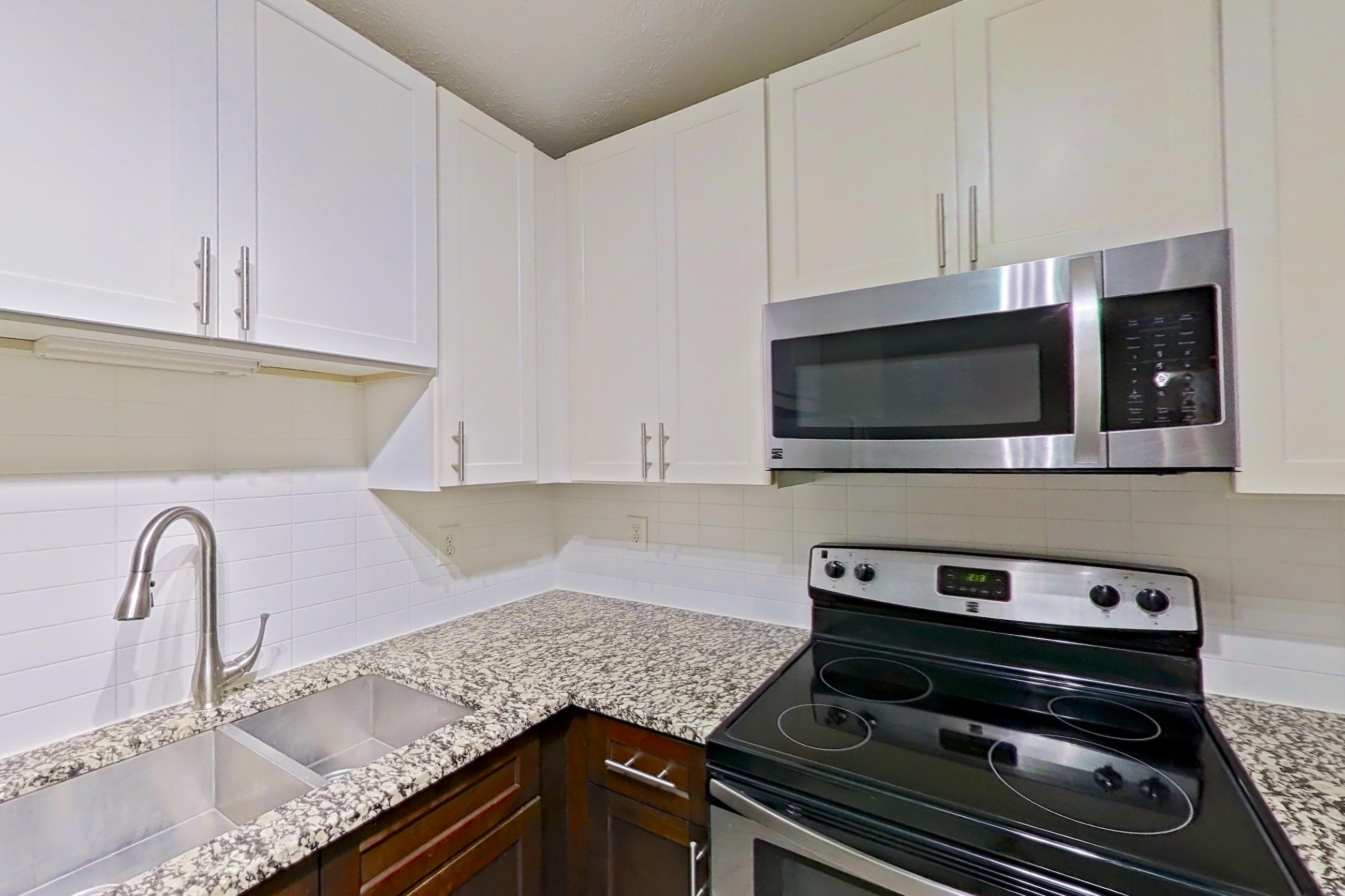 Kitchen with electric range, light countertops, light stone countertops, light wood-finish flooring, microwave, oven/range, refrigerator, and stainless steel appliances, Apartment 2165S at Cortland at the Village