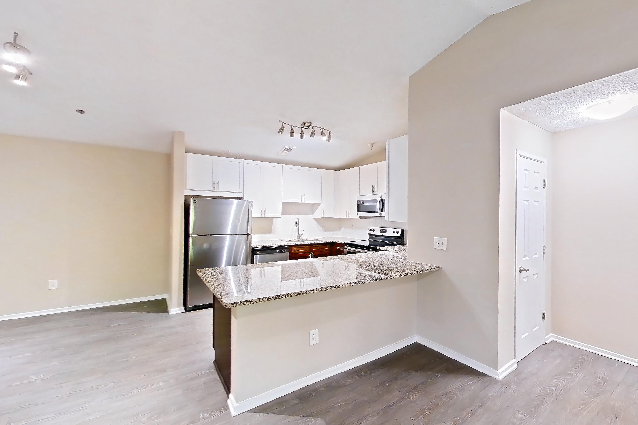 Living room with dark wood-finish flooring, dishwasher, electric range, light countertops, light stone countertops, light wood-finish flooring, oven/range, refrigerator, and stainless steel appliances, Apartment 2165S at Cortland at the Village