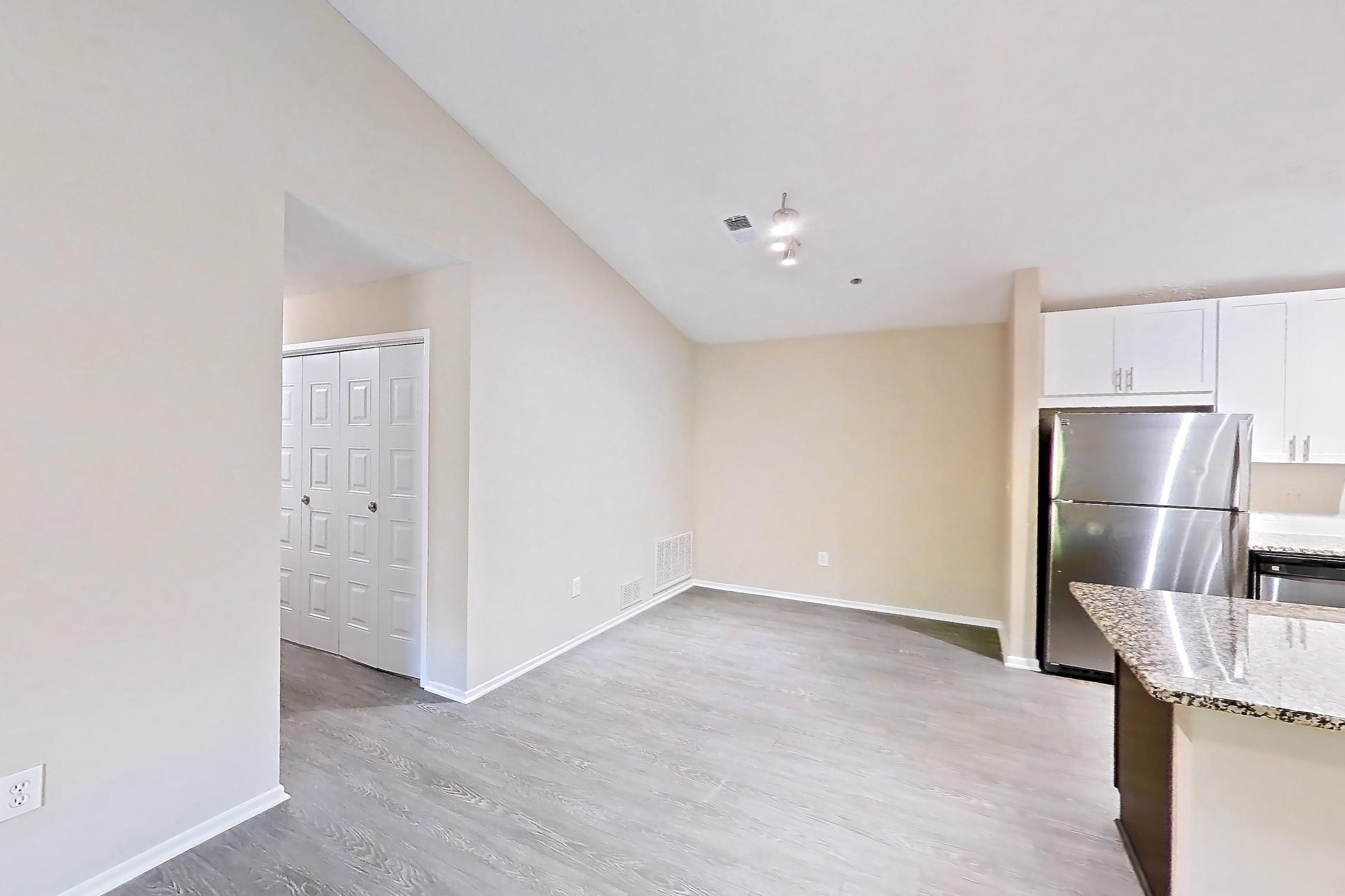 Living room with dark wood-finish flooring, dishwasher, electric range, light countertops, light stone countertops, light wood-finish flooring, oven/range, refrigerator, and stainless steel appliances, Apartment 2165S at Cortland at the Village