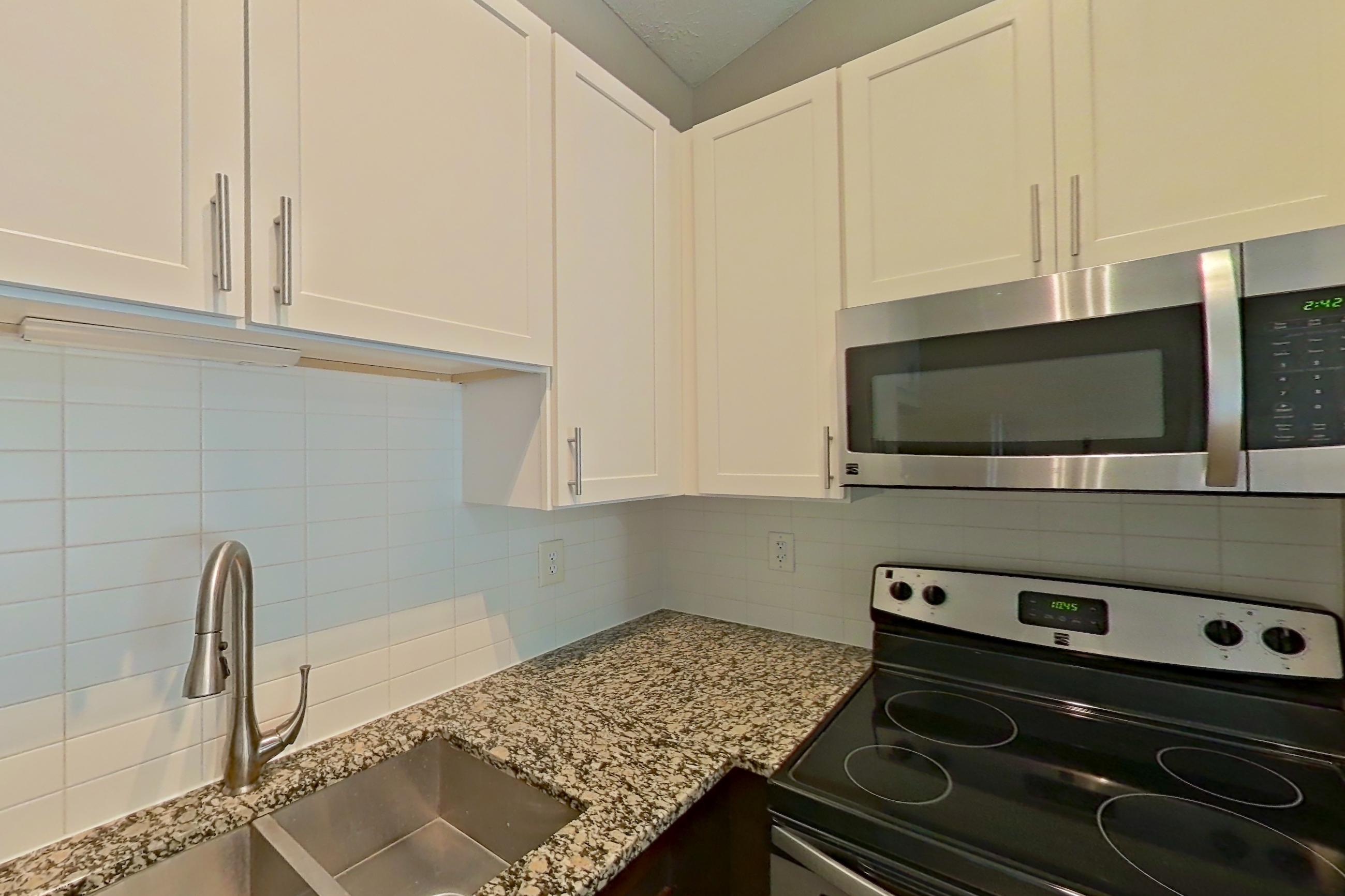 Kitchen with dishwasher, electric range, light countertops, light stone countertops, light wood-finish flooring, microwave, oven/range, refrigerator, and stainless steel appliances, Apartment 2167L at Cortland at the Village