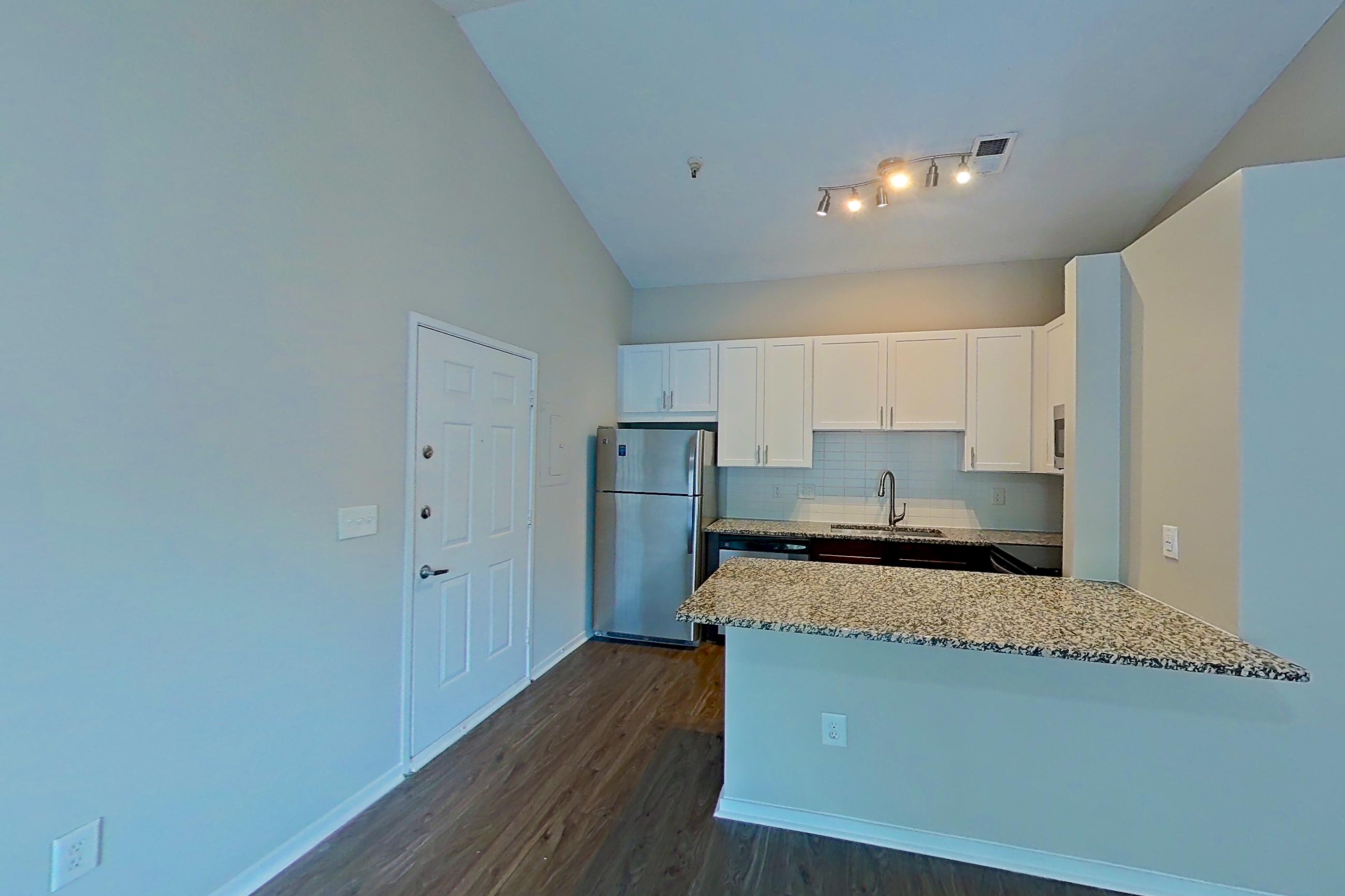 Living room with dark wood-finish flooring, dishwasher, light stone countertops, refrigerator, and stainless steel appliances, Apartment 2167L at Cortland at the Village