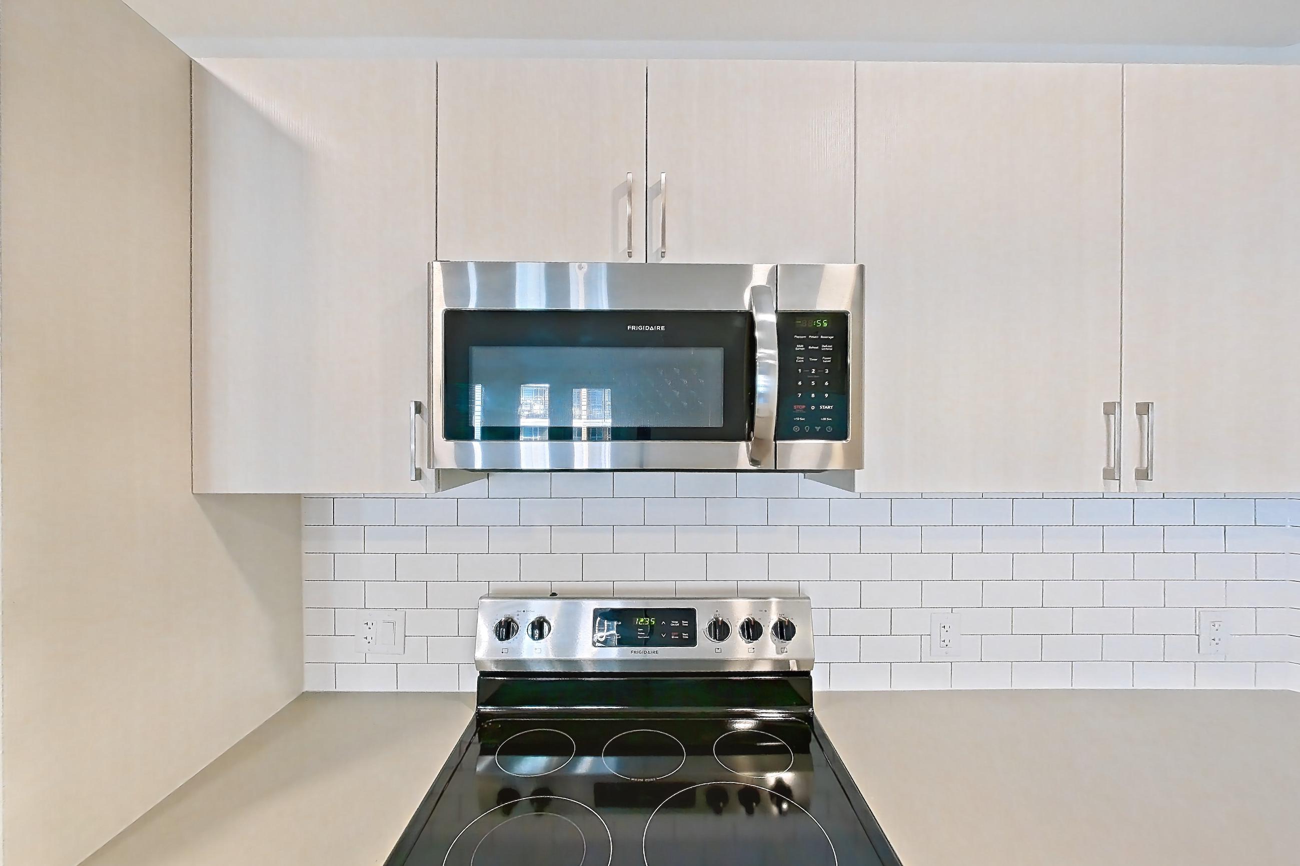 Kitchen with dishwasher, electric range, light countertops, light wood-finish flooring, microwave, oven/range, refrigerator, and stainless steel appliances, Apartment 425 at Braxton
