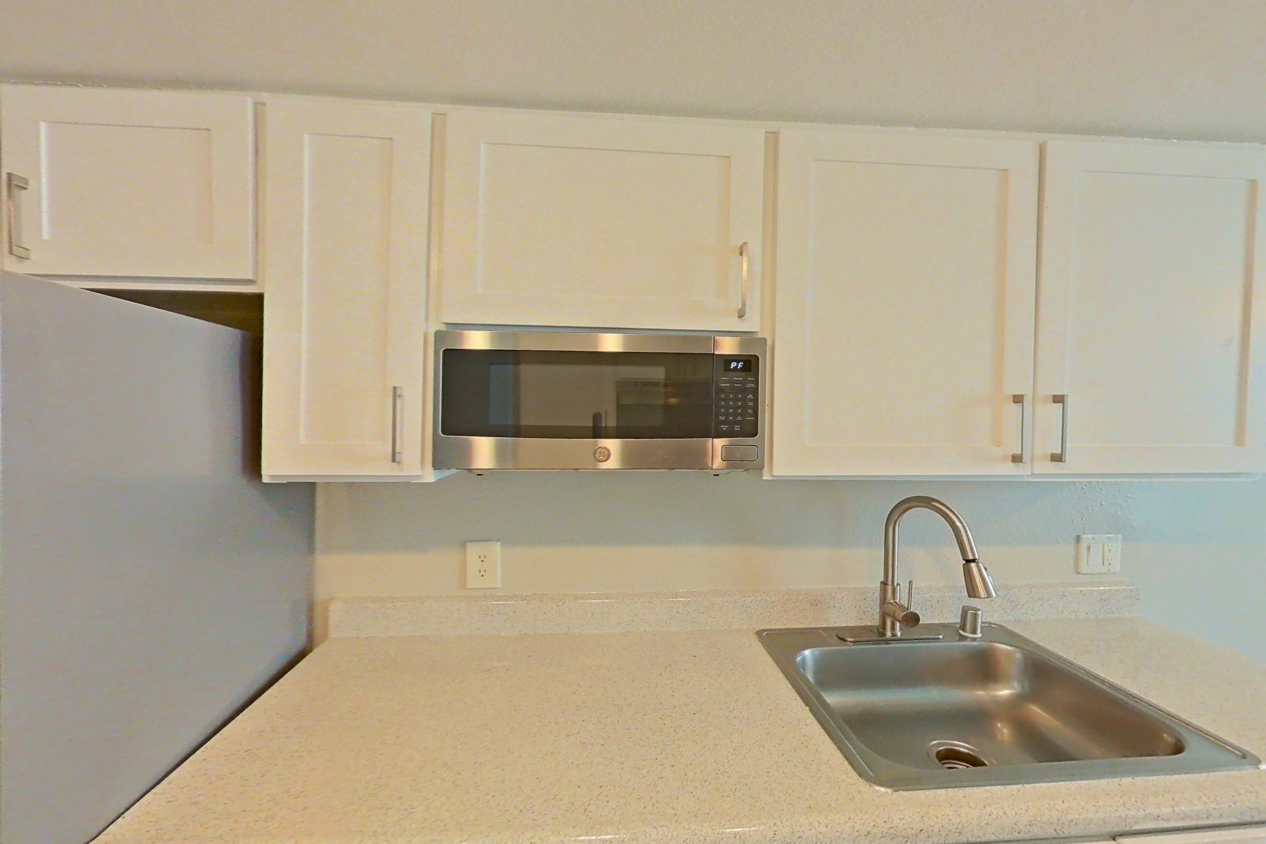 Kitchen with dishwasher, electric range, light countertops, light stone countertops, light wood-finish flooring, microwave, oven/range, range hood, refrigerator, and stainless steel appliances, Apartment 03 at Avana Rancho Cucamonga
