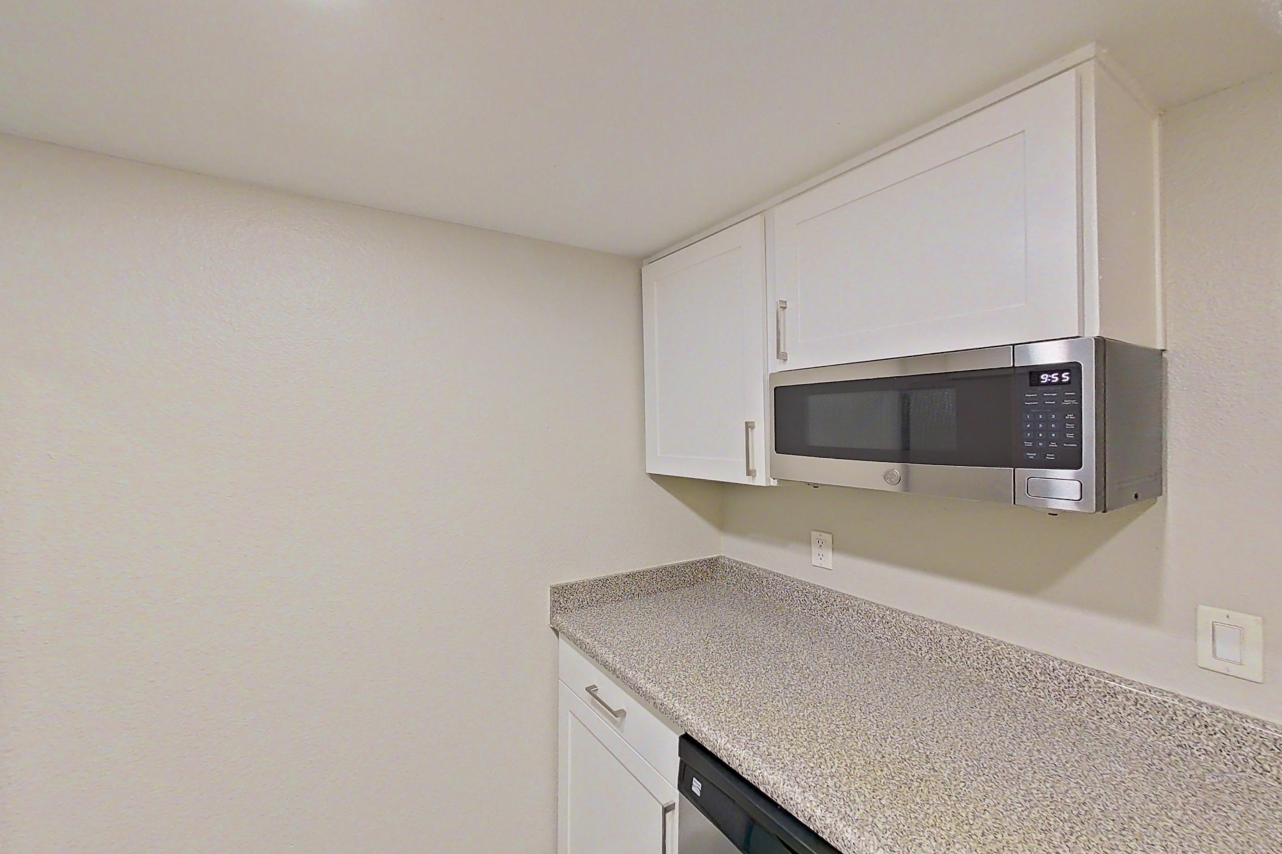 Kitchen with dishwasher, electric range, light countertops, light stone countertops, light wood-finish flooring, oven/range, refrigerator, and stainless steel appliances, Apartment 12 at Avana Rancho Cucamonga