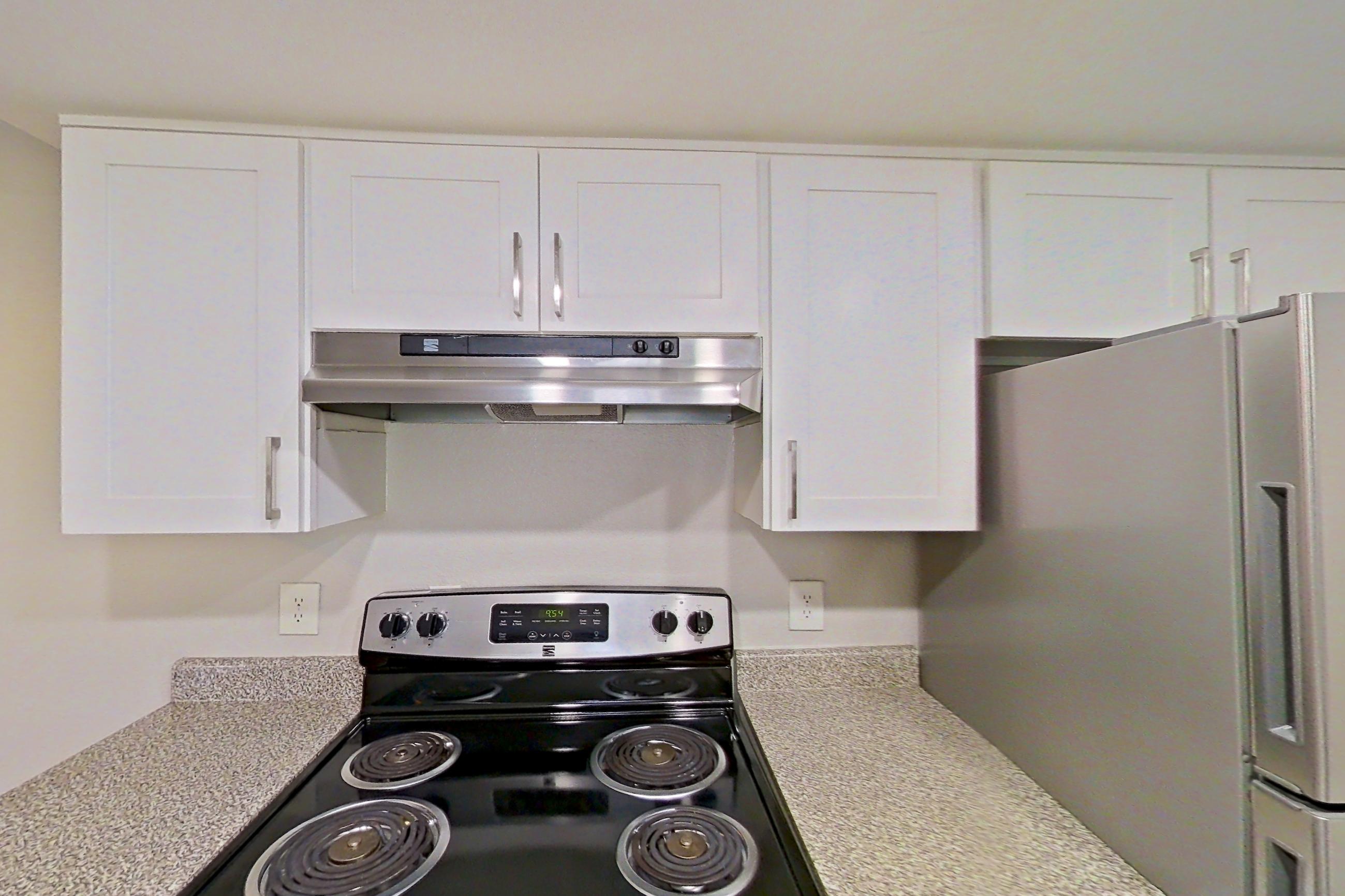 Kitchen with dishwasher, electric range, light countertops, light stone countertops, light wood-finish flooring, oven/range, refrigerator, and stainless steel appliances, Apartment 12 at Avana Rancho Cucamonga