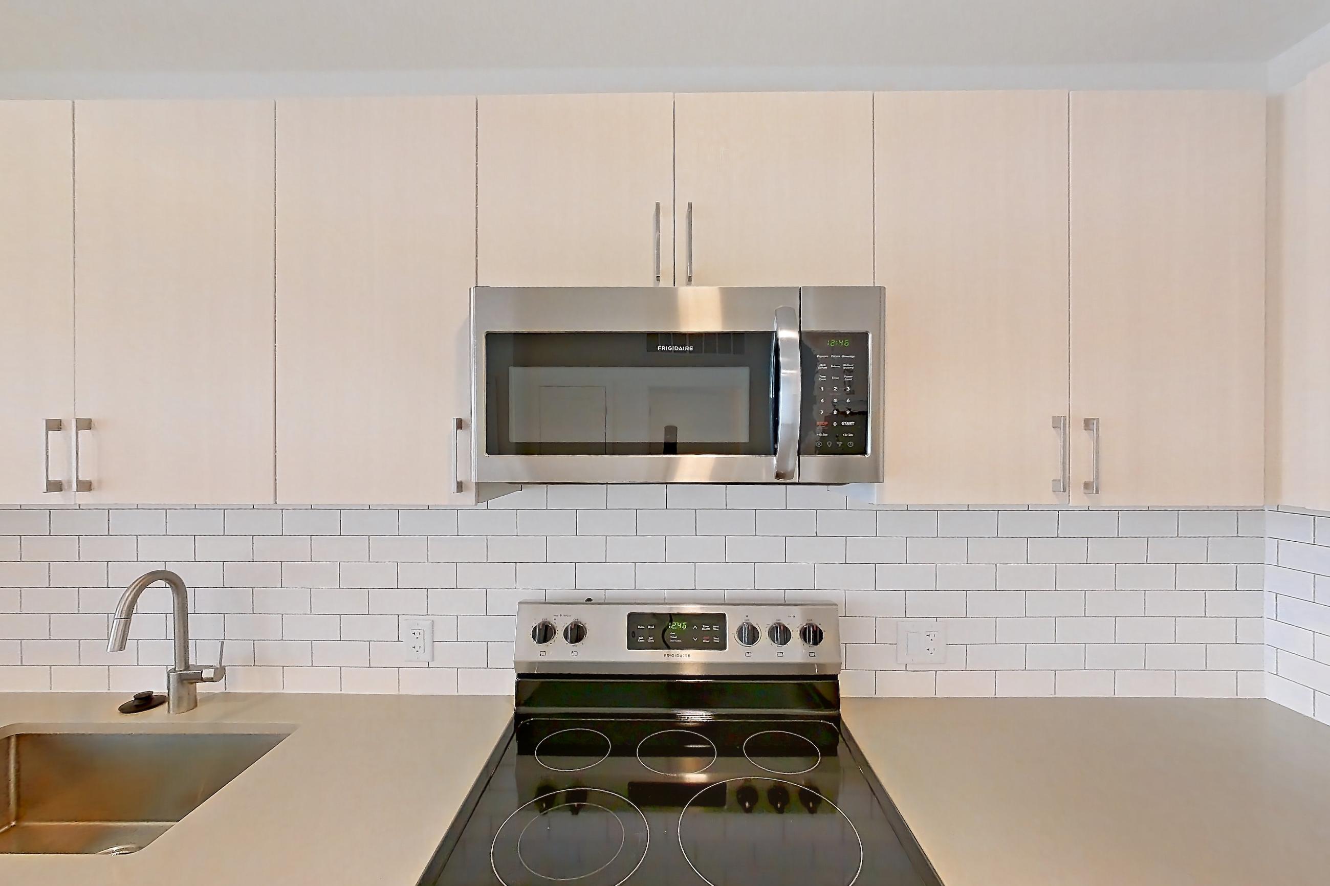 Kitchen with dishwasher, electric range, light countertops, light wood-finish flooring, microwave, oven/range, refrigerator, and stainless steel appliances, Apartment 440 at Braxton