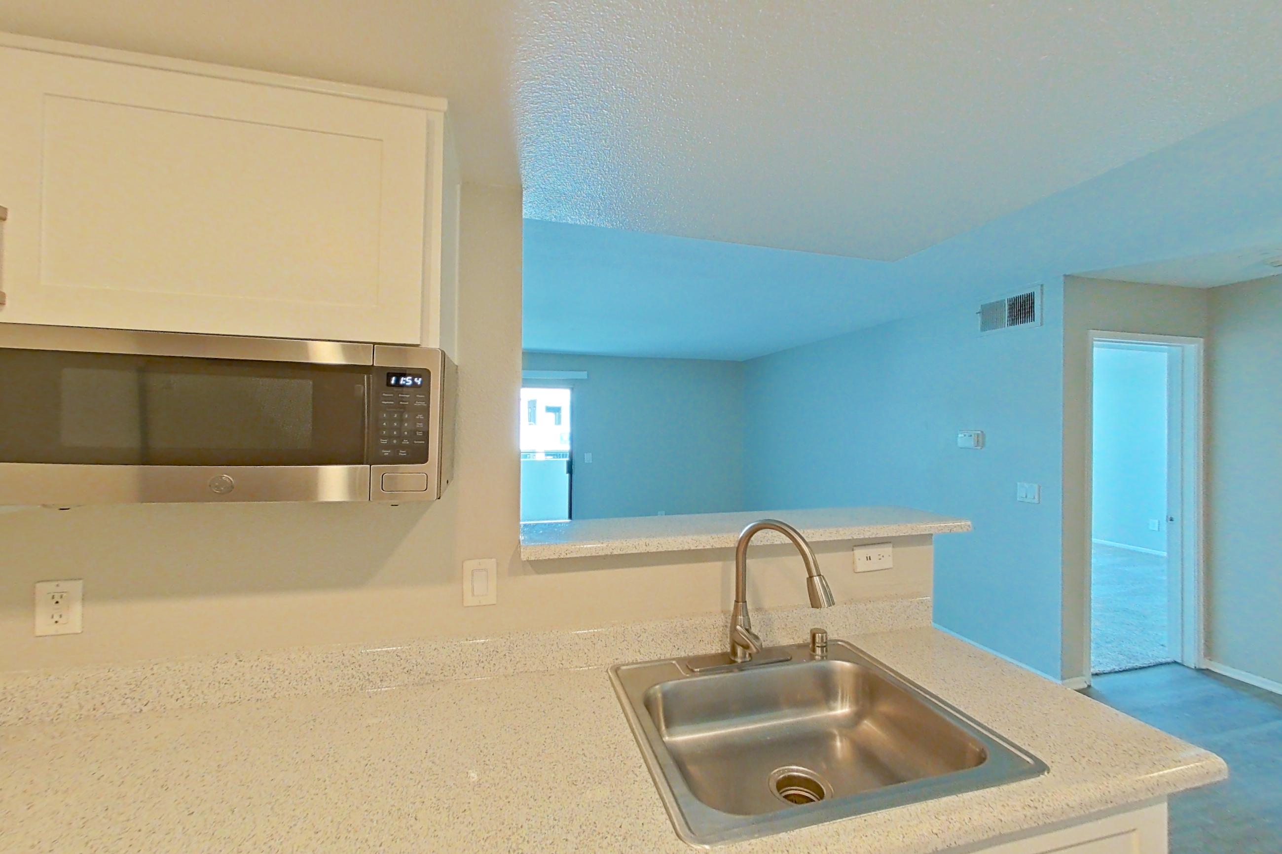 Kitchen with dishwasher, electric range, light countertops, light stone countertops, light wood-finish flooring, microwave, oven/range, and stainless steel appliances, Apartment 21 at Avana Rancho Cucamonga
