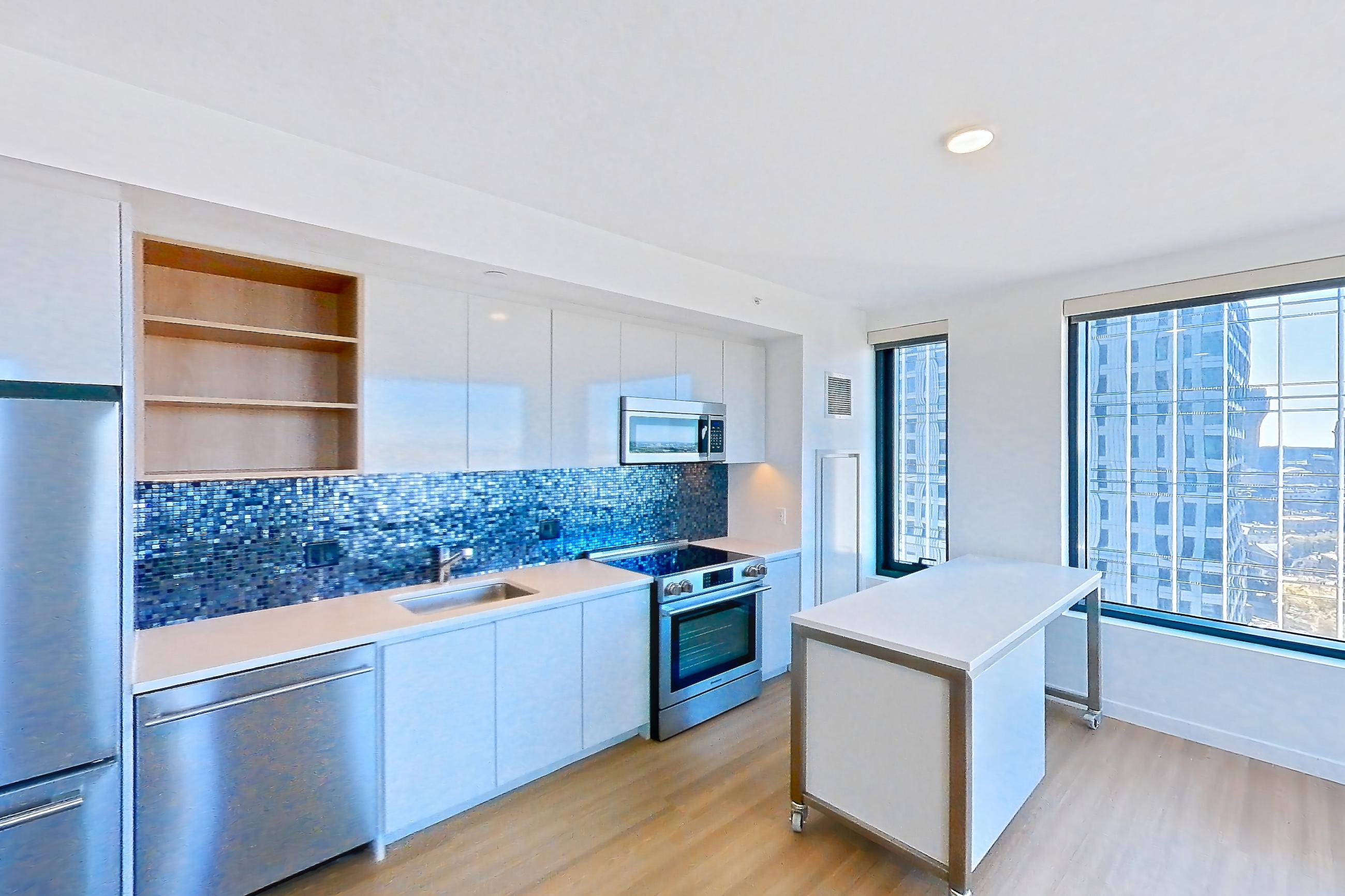 Living room with dishwasher, electric range, light stone countertops, light wood-finish flooring, oven/range, refrigerator, and stainless steel appliances, Apartment 2402 at The Sudbury