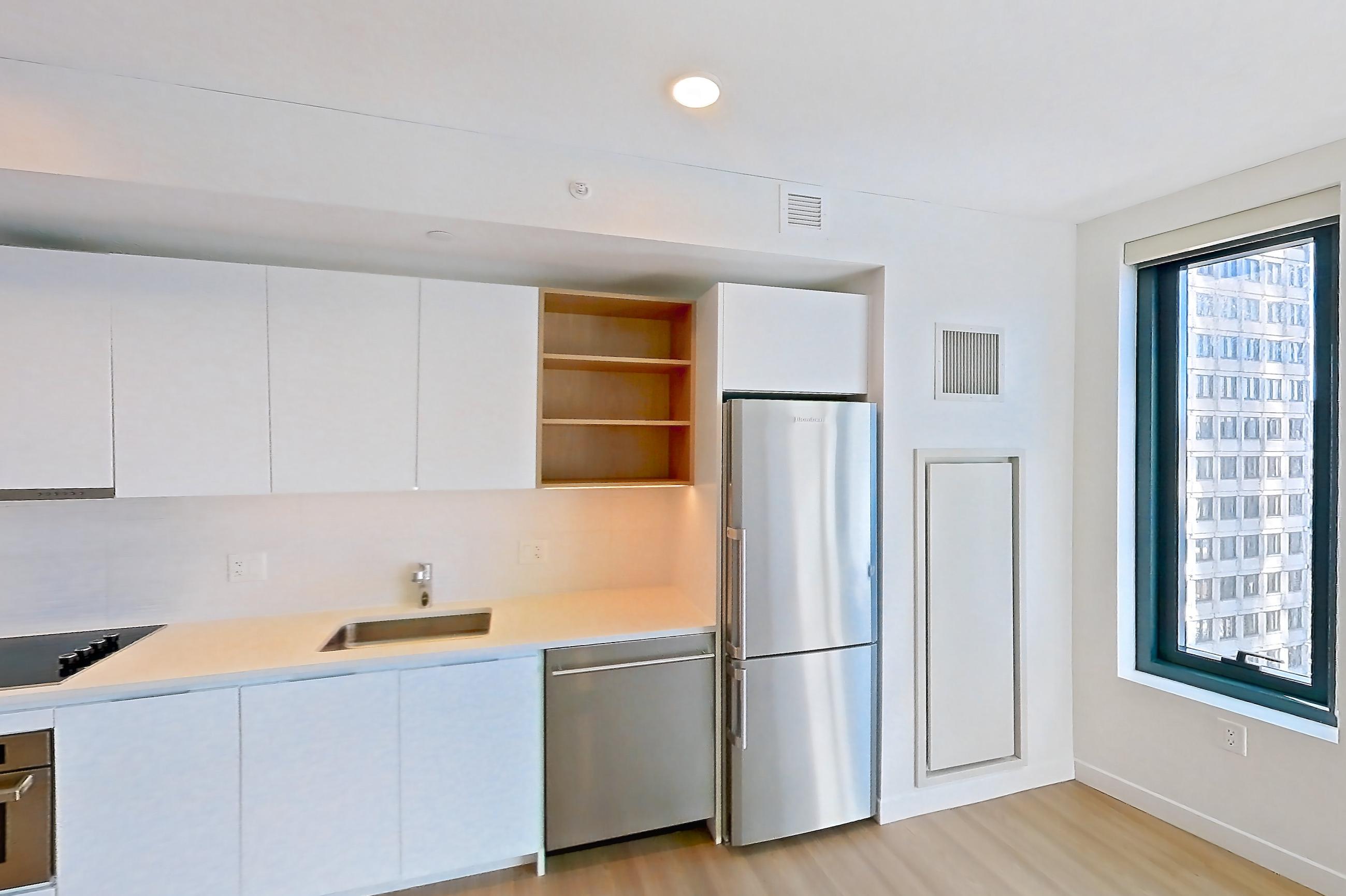Kitchen with black appliances, cooktop, dishwasher, electric cooktop, light countertops, light wood-finish flooring, oven/range, refrigerator, stainless steel appliances, and white appliances, Apartment 1114 at The Sudbury