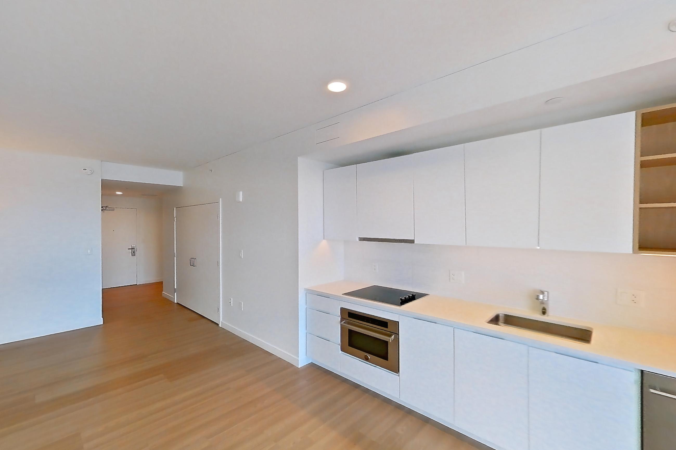 Kitchen with black appliances, cooktop, dishwasher, electric cooktop, light countertops, light wood-finish flooring, oven/range, refrigerator, stainless steel appliances, and white appliances, Apartment 1114 at The Sudbury