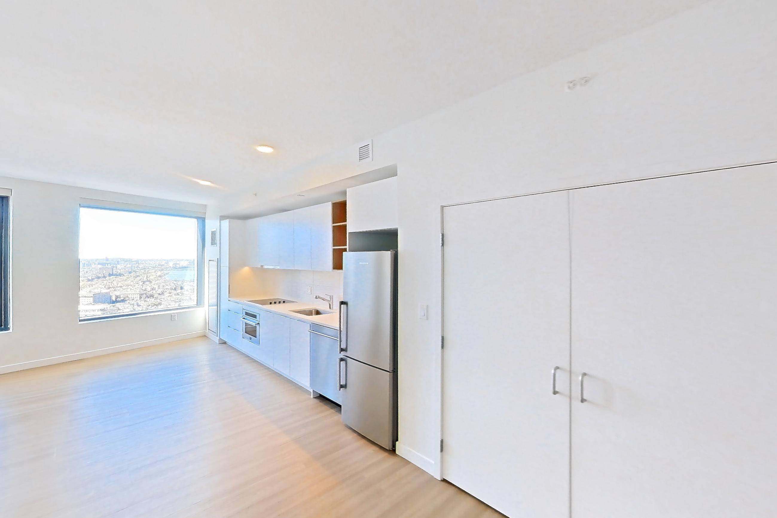 Living room with light wood-finish flooring and refrigerator, Apartment 2812 at The Sudbury