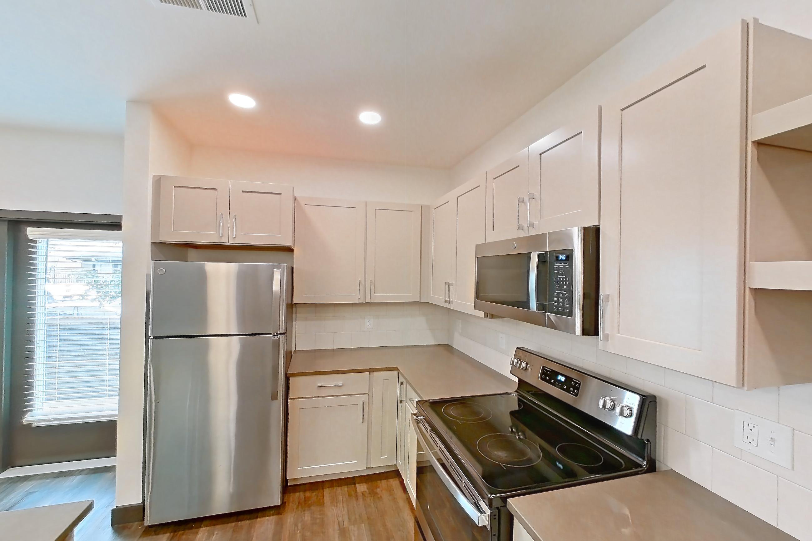 Kitchen with dark countertops, dark wood-finish flooring, dishwasher, gas range, oven/range, and stainless steel appliances, Apartment 3102 at The Grounds
