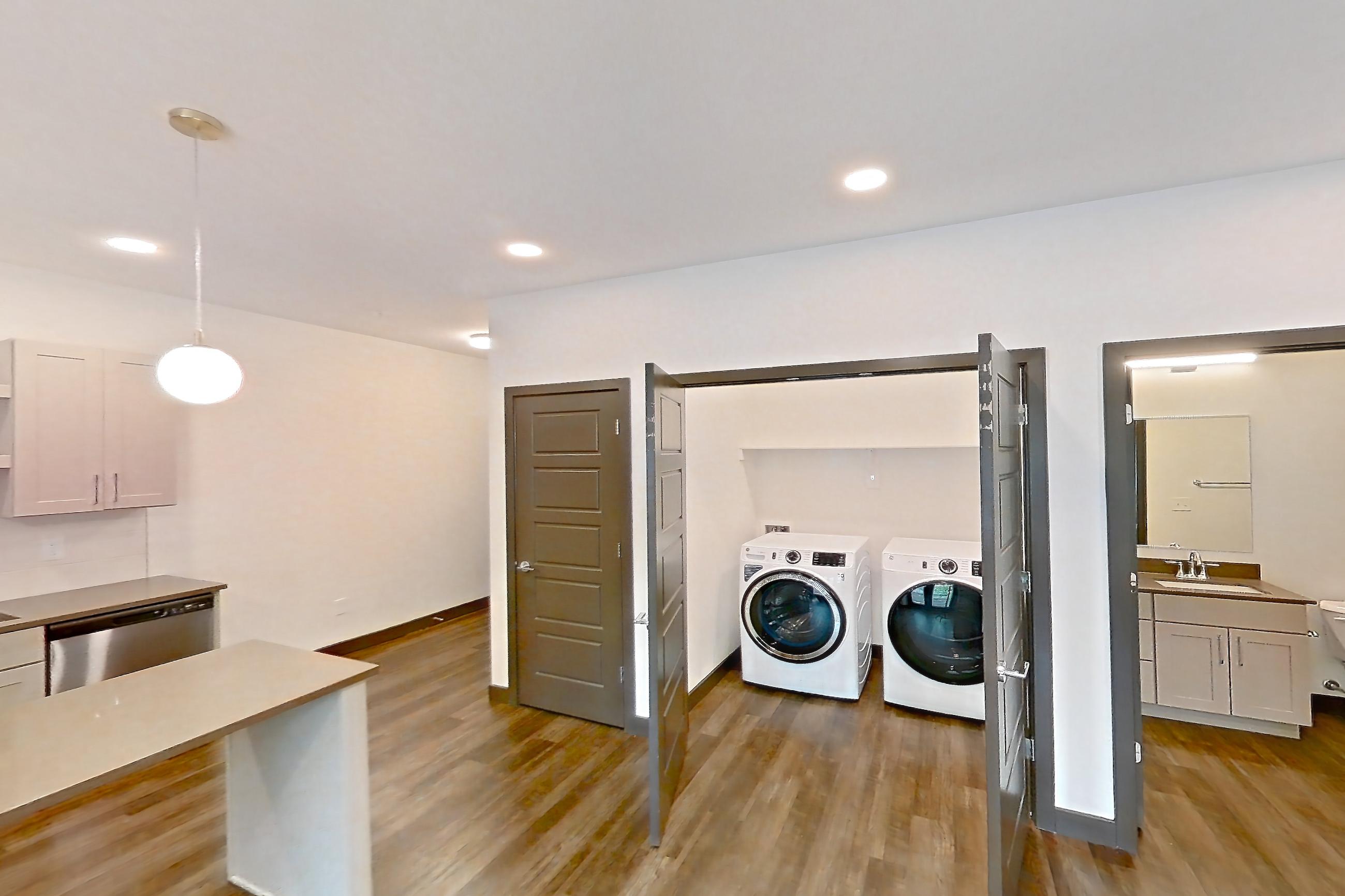 Living room with dark wood-finish flooring, dishwasher, electric range, in-unit laundry, light countertops, microwave, oven/range, stainless steel appliances, and white appliances, Apartment 3102 at The Grounds