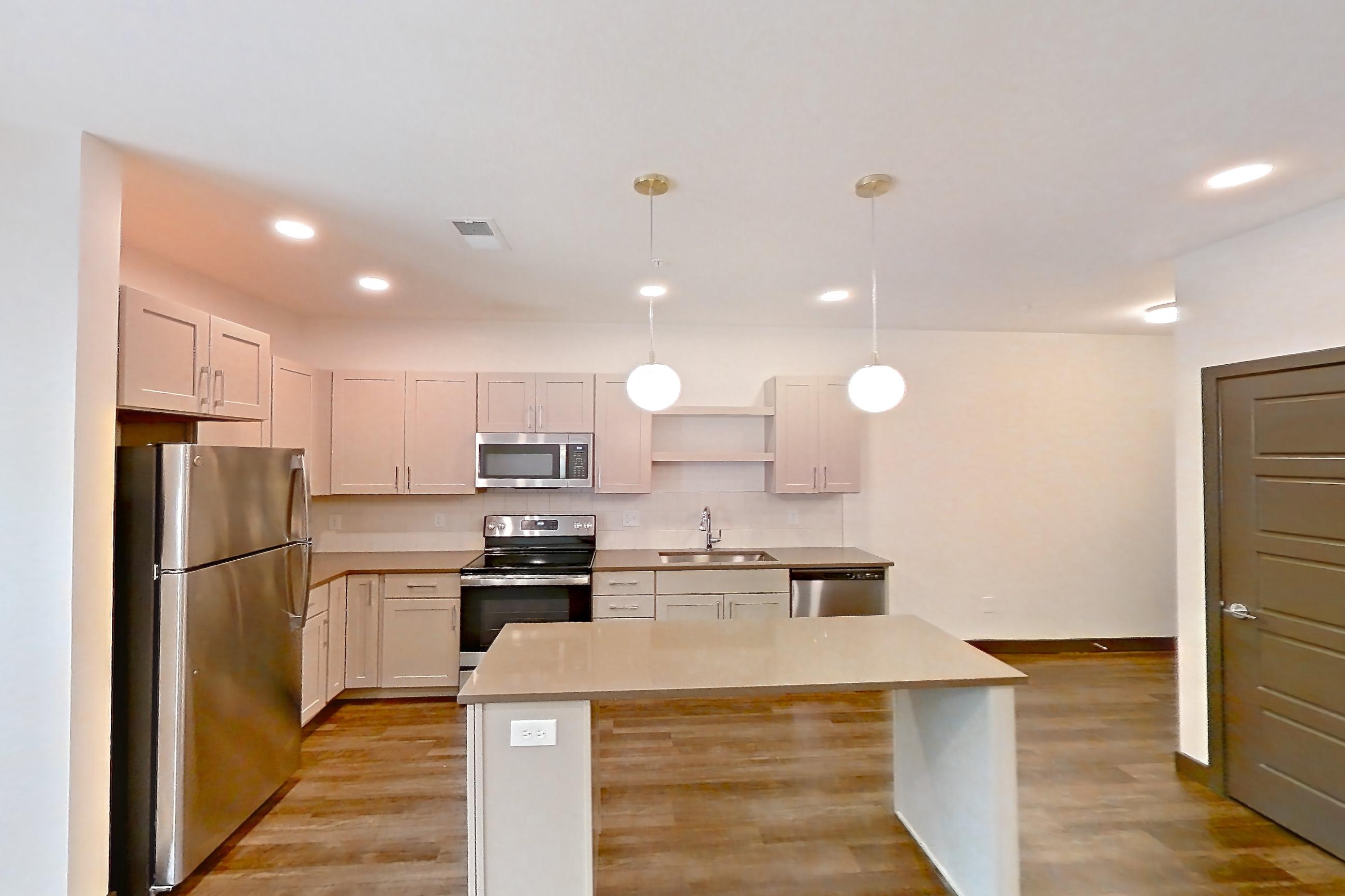 Living room with dark wood-finish flooring, dishwasher, electric range, in-unit laundry, light countertops, microwave, oven/range, stainless steel appliances, and white appliances, Apartment 3102 at The Grounds