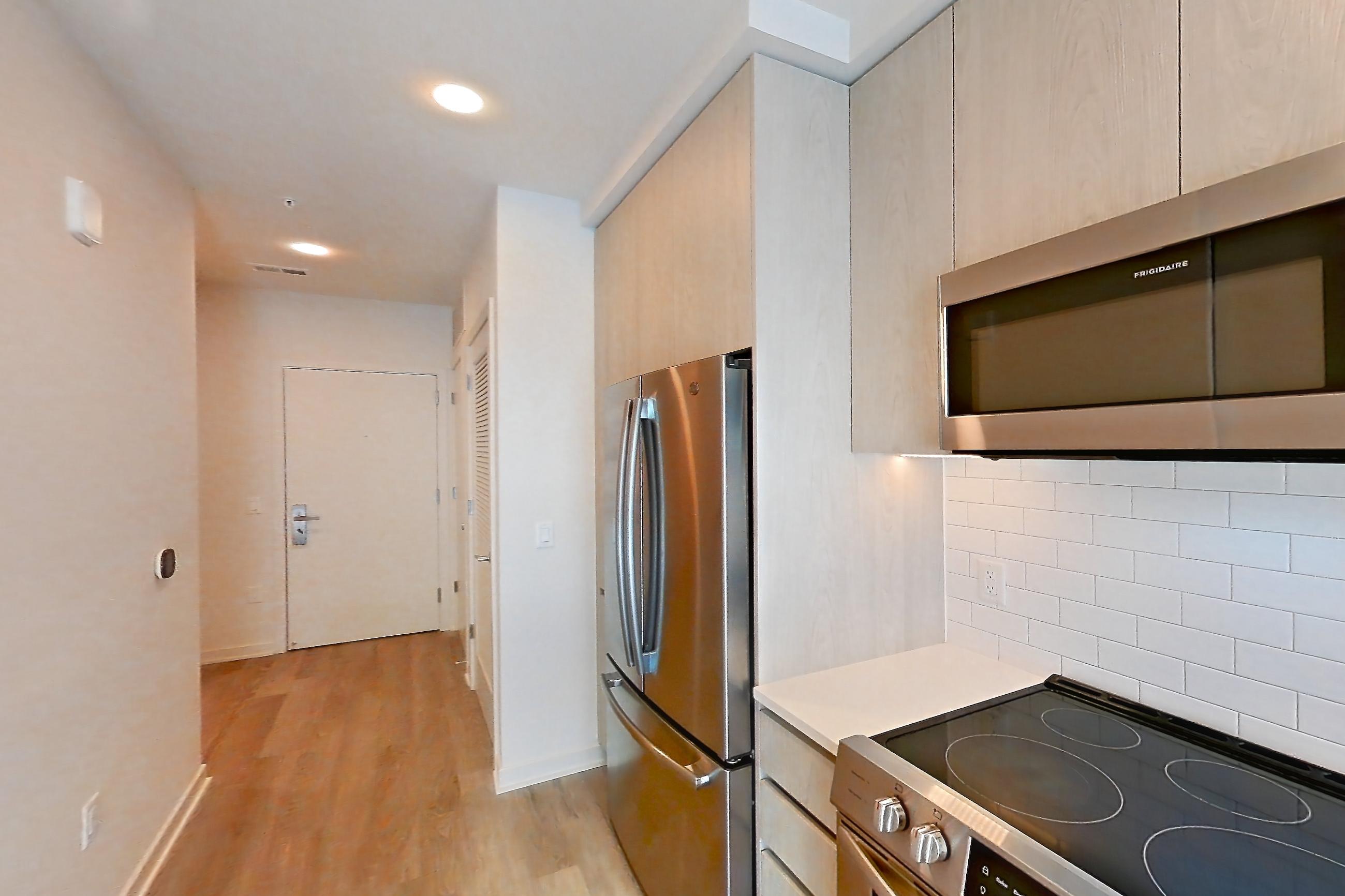 Kitchen with dishwasher, electric range, light countertops, light stone countertops, light wood-finish flooring, microwave, oven/range, refrigerator, and stainless steel appliances, Apartment 3421 at Platform (VA)