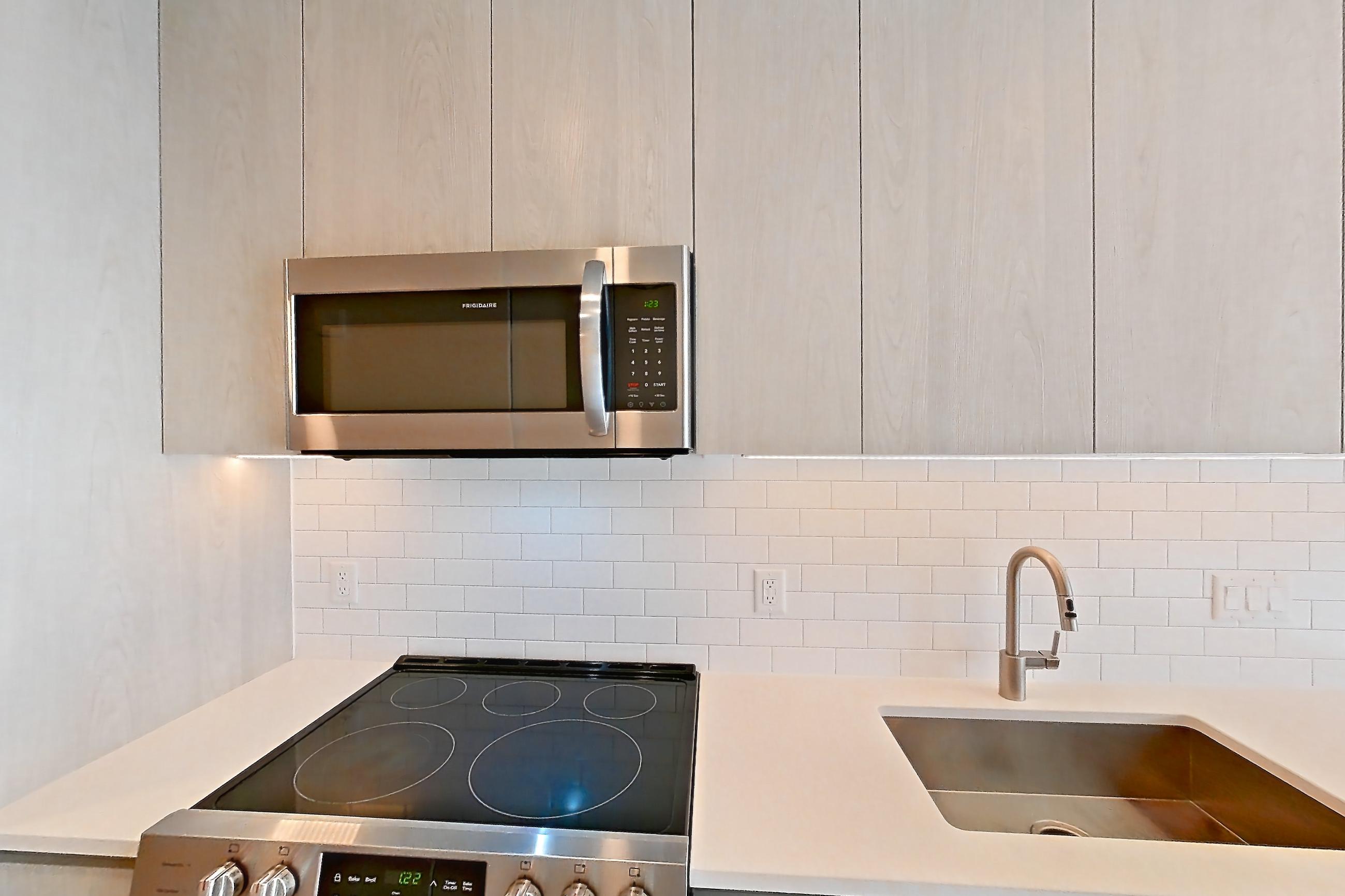 Kitchen with dishwasher, electric range, light countertops, light stone countertops, light wood-finish flooring, microwave, oven/range, refrigerator, and stainless steel appliances, Apartment 3421 at Platform (VA)