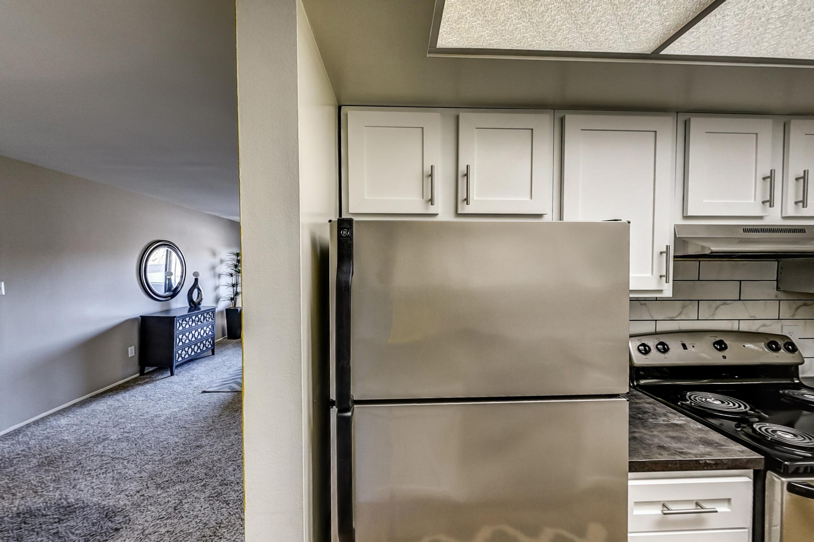 Kitchen with dark countertops, electric range, light wood-finish flooring, oven/range, refrigerator, and stainless steel appliances, Apartment Model 1 at Canterbury Green