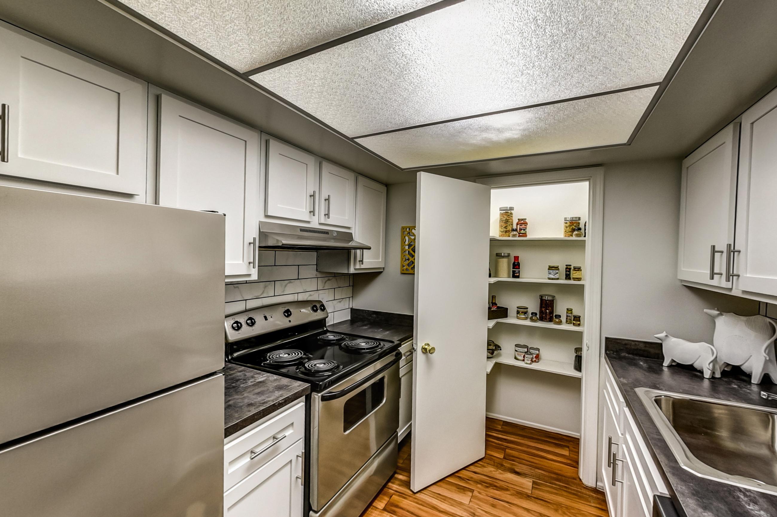 Kitchen with dark countertops, electric range, light wood-finish flooring, oven/range, refrigerator, and stainless steel appliances, Apartment Model 1 at Canterbury Green