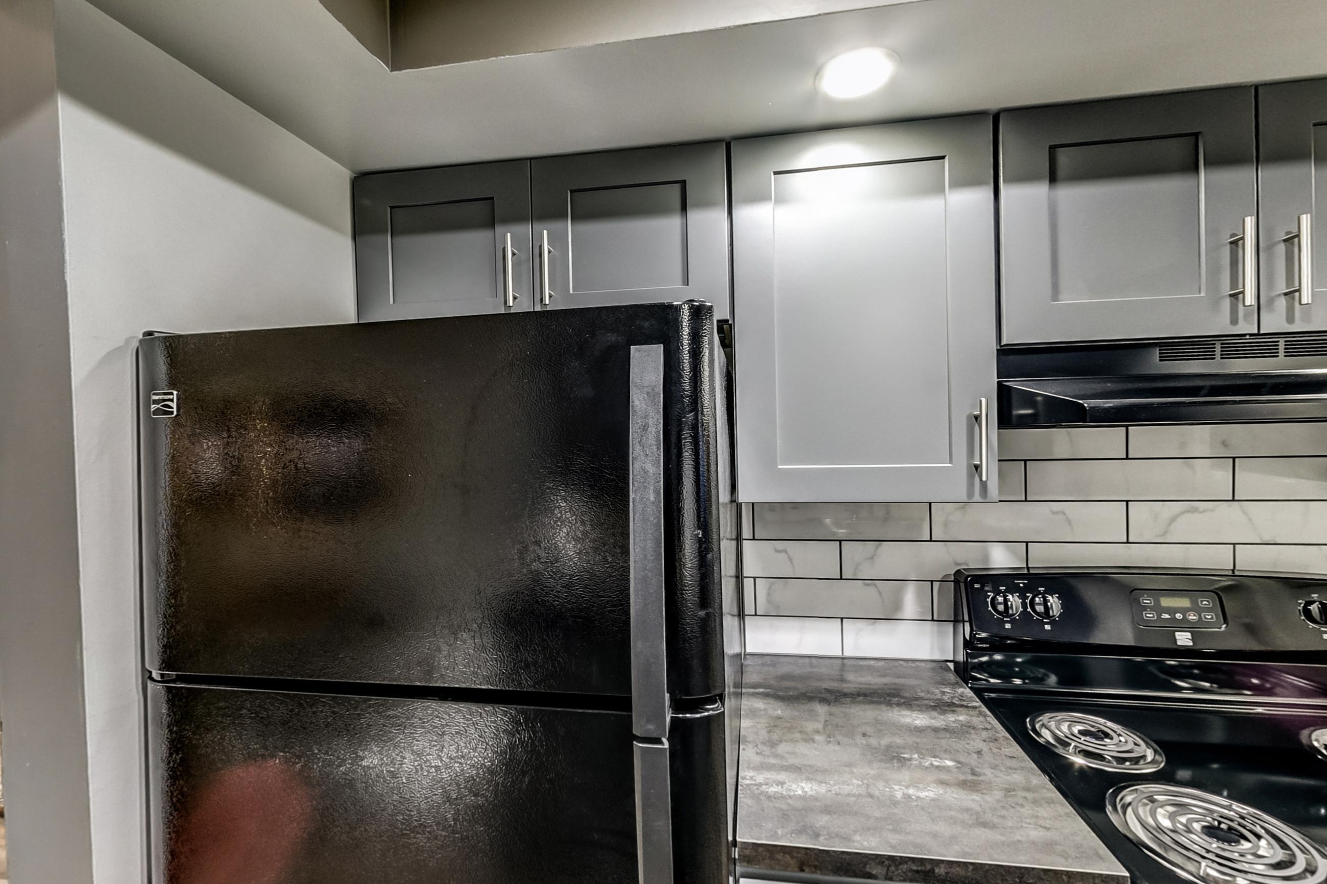 Kitchen with black appliances, dark countertops, dishwasher, electric range, light wood-finish flooring, oven/range, range hood, and refrigerator, Apartment Model 3 at Canterbury Green