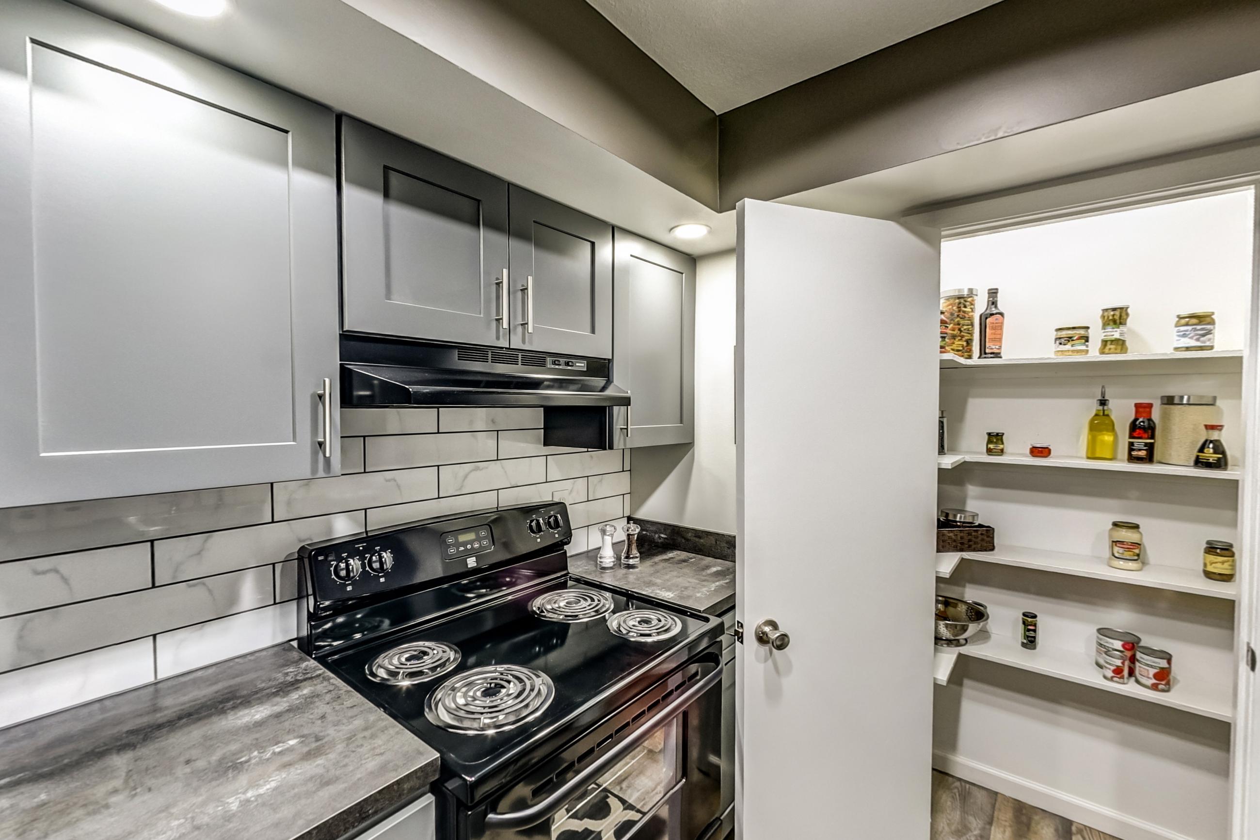 Kitchen with black appliances, dark countertops, dishwasher, electric range, light wood-finish flooring, oven/range, range hood, and refrigerator, Apartment Model 3 at Canterbury Green