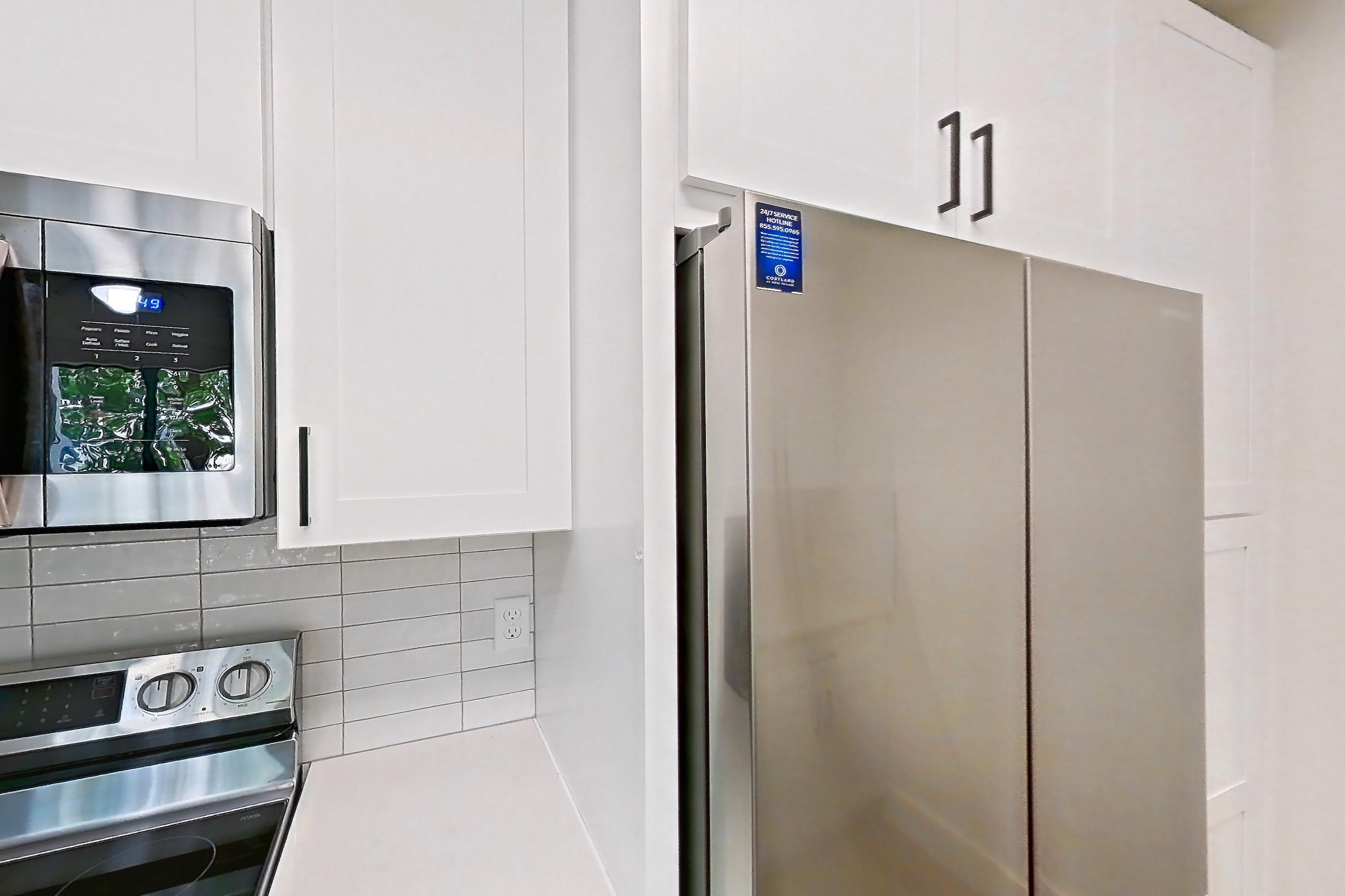Kitchen with dishwasher, electric range, light countertops, light stone countertops, light wood-finish flooring, microwave, oven/range, refrigerator, and stainless steel appliances, Apartment 319 at Cortland at West Village