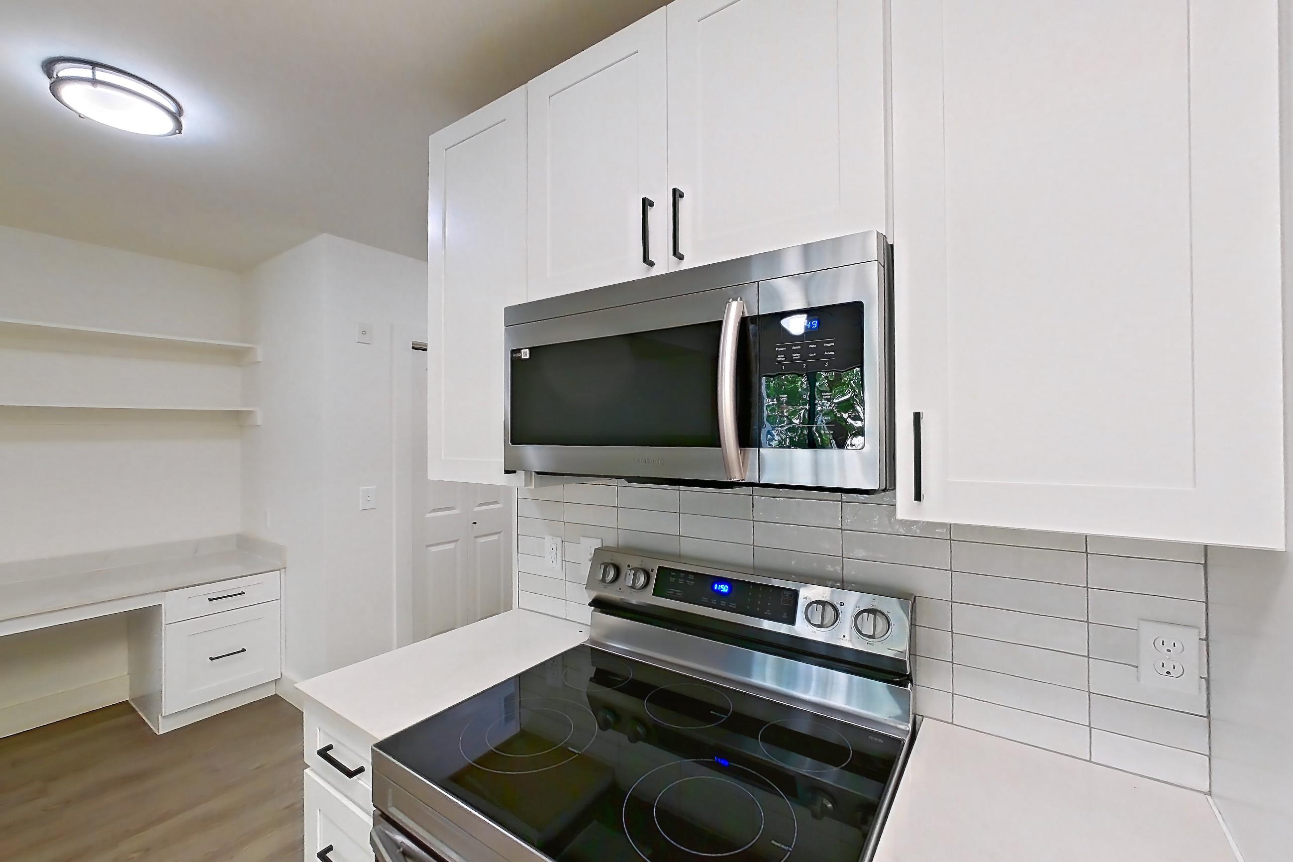 Kitchen with dishwasher, electric range, light countertops, light stone countertops, light wood-finish flooring, microwave, oven/range, refrigerator, and stainless steel appliances, Apartment 319 at Cortland at West Village