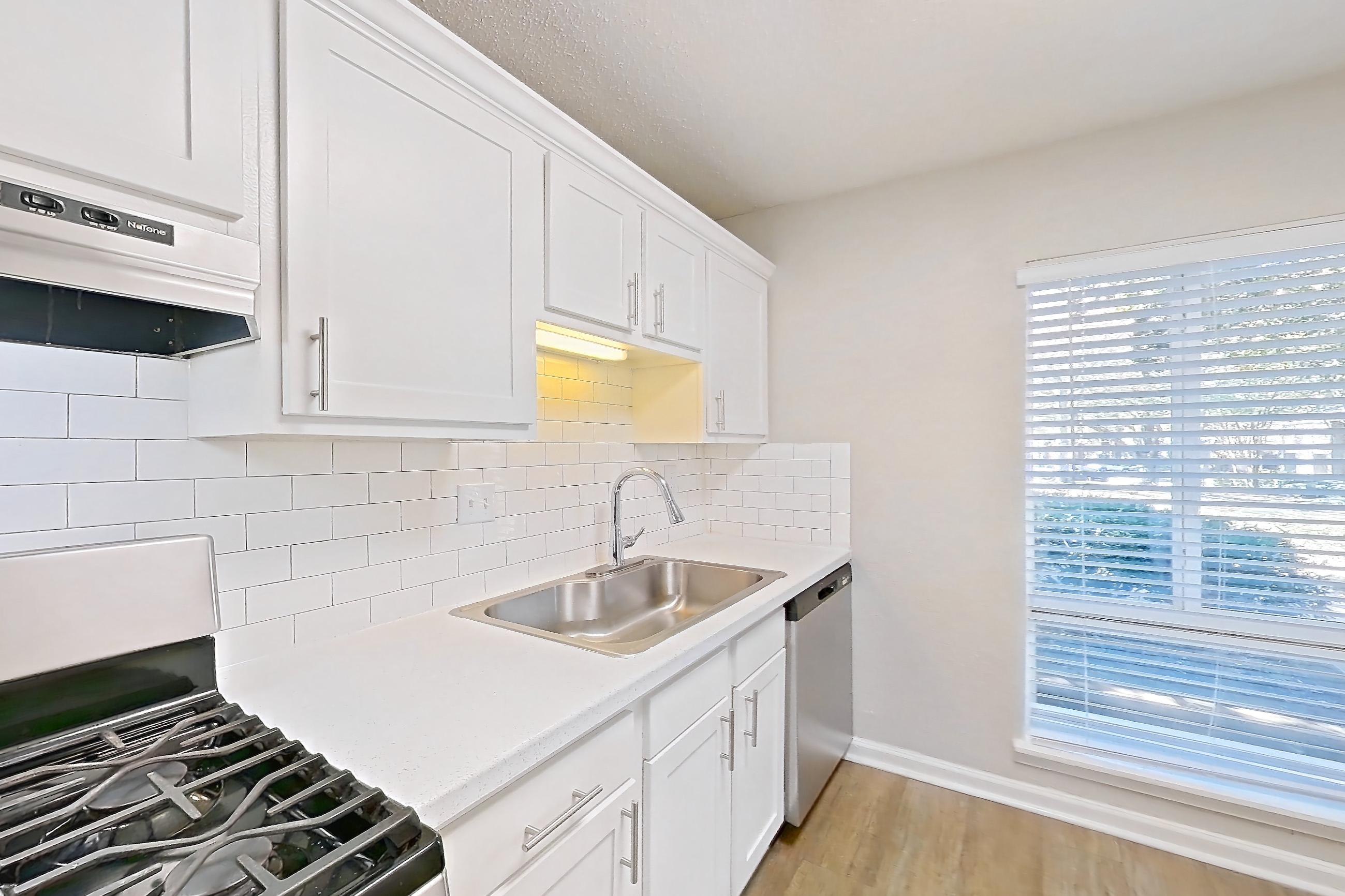 Kitchen with dishwasher, gas range, light countertops, light stone countertops, light wood-finish flooring, oven/range, range hood, refrigerator, and stainless steel appliances, Apartment H1456T at The Legacy at Druid Hills