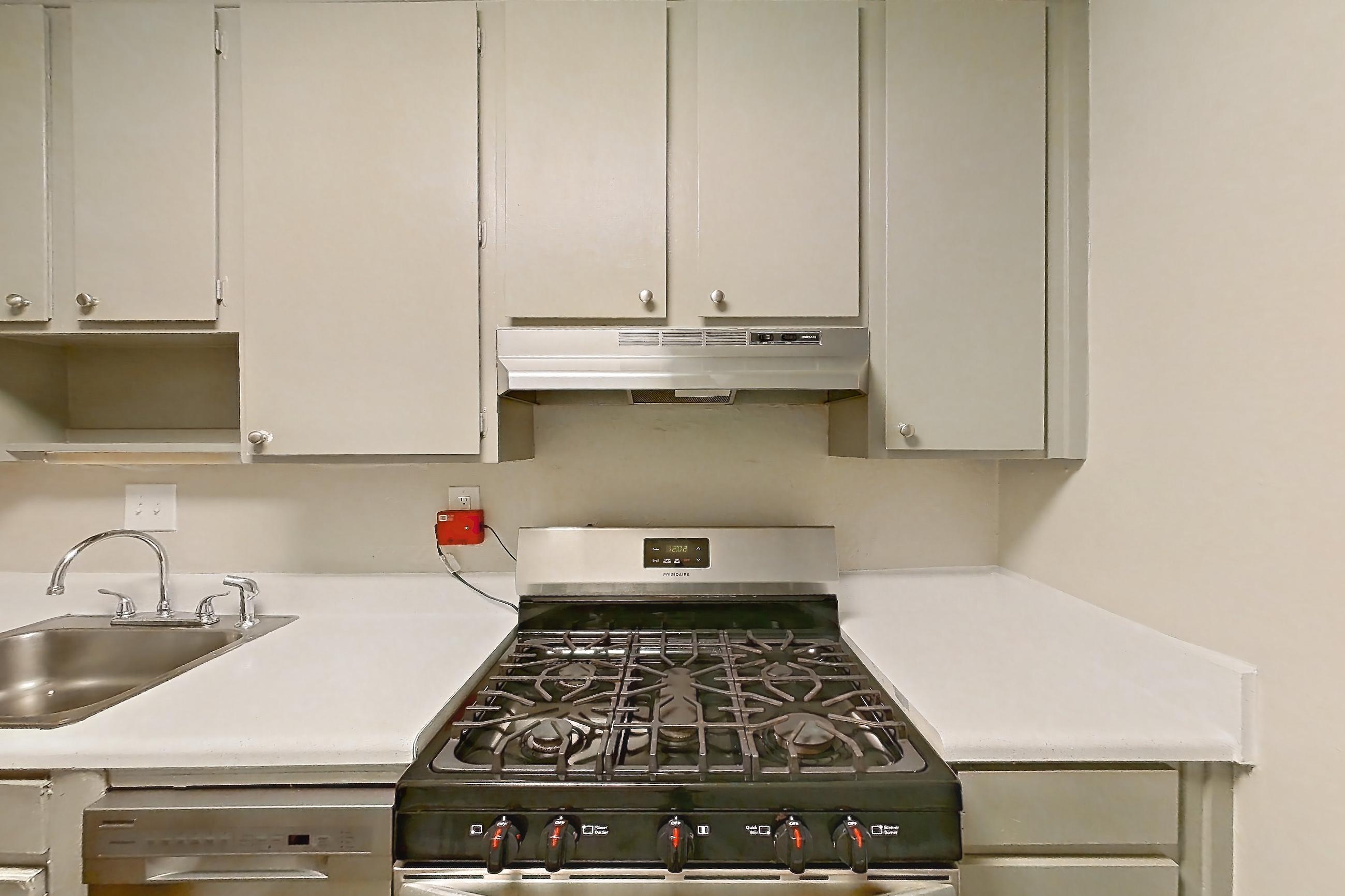 Kitchen with dishwasher, gas range, light countertops, light wood-finish flooring, oven/range, refrigerator, and stainless steel appliances, Apartment H1525F at The Legacy at Druid Hills