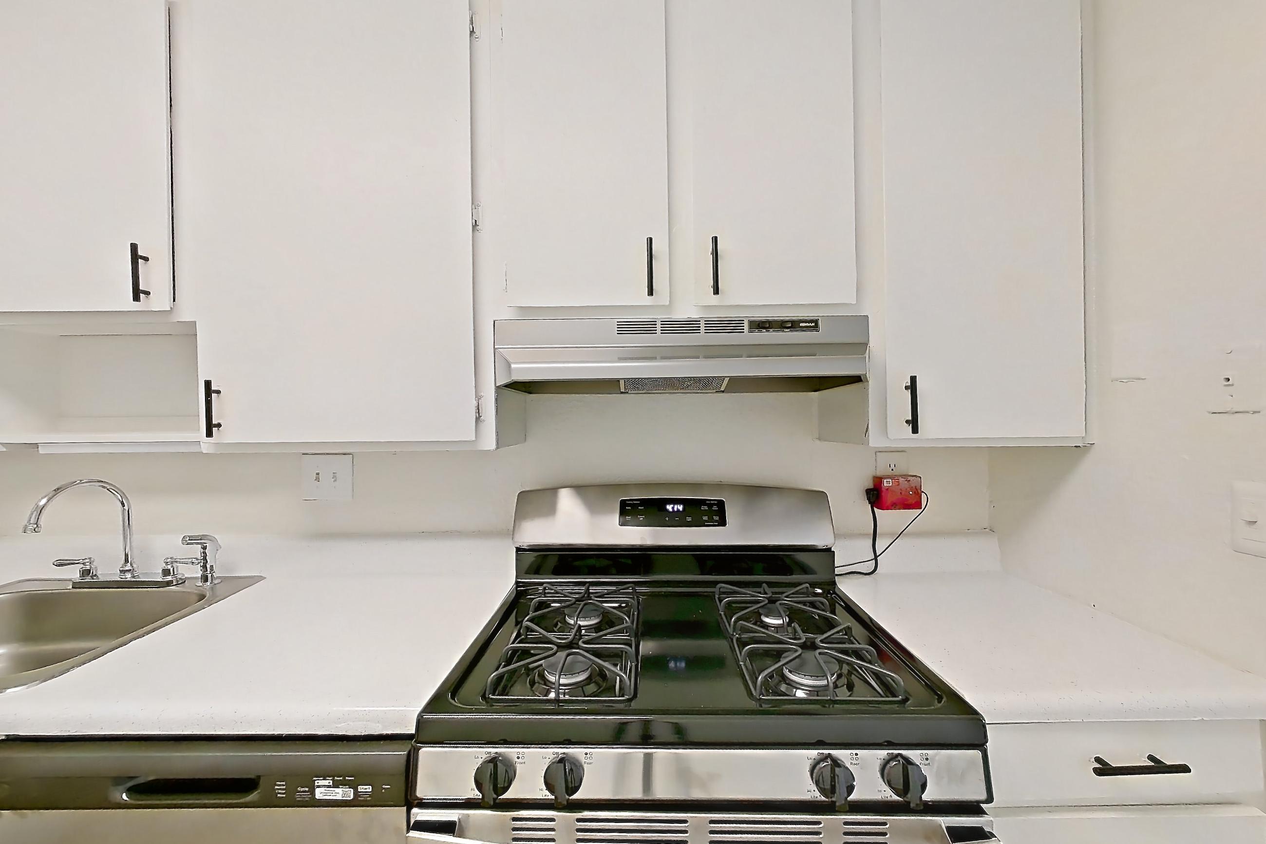 Kitchen with dishwasher, gas range, light countertops, light wood-finish flooring, oven/range, range hood, refrigerator, and stainless steel appliances, Apartment H1536D at The Legacy at Druid Hills