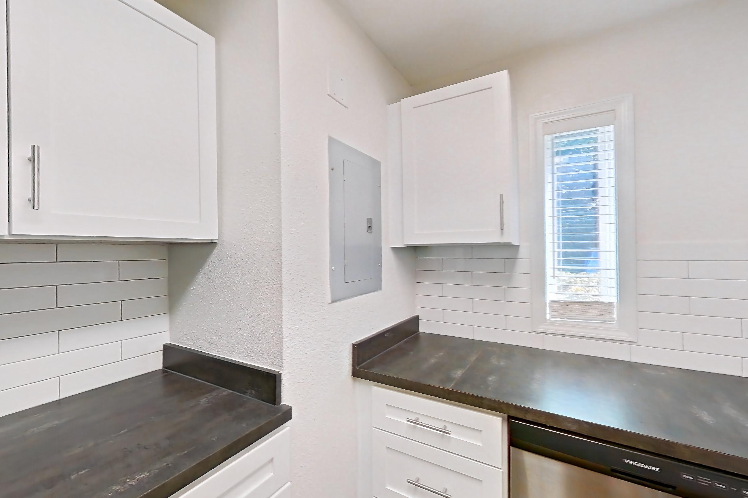 Kitchen with black appliances, dark countertops, dishwasher, electric range, light countertops, light wood-finish flooring, oven/range, range hood, refrigerator, and stainless steel appliances, Apartment L1452T at The Legacy at Druid Hills