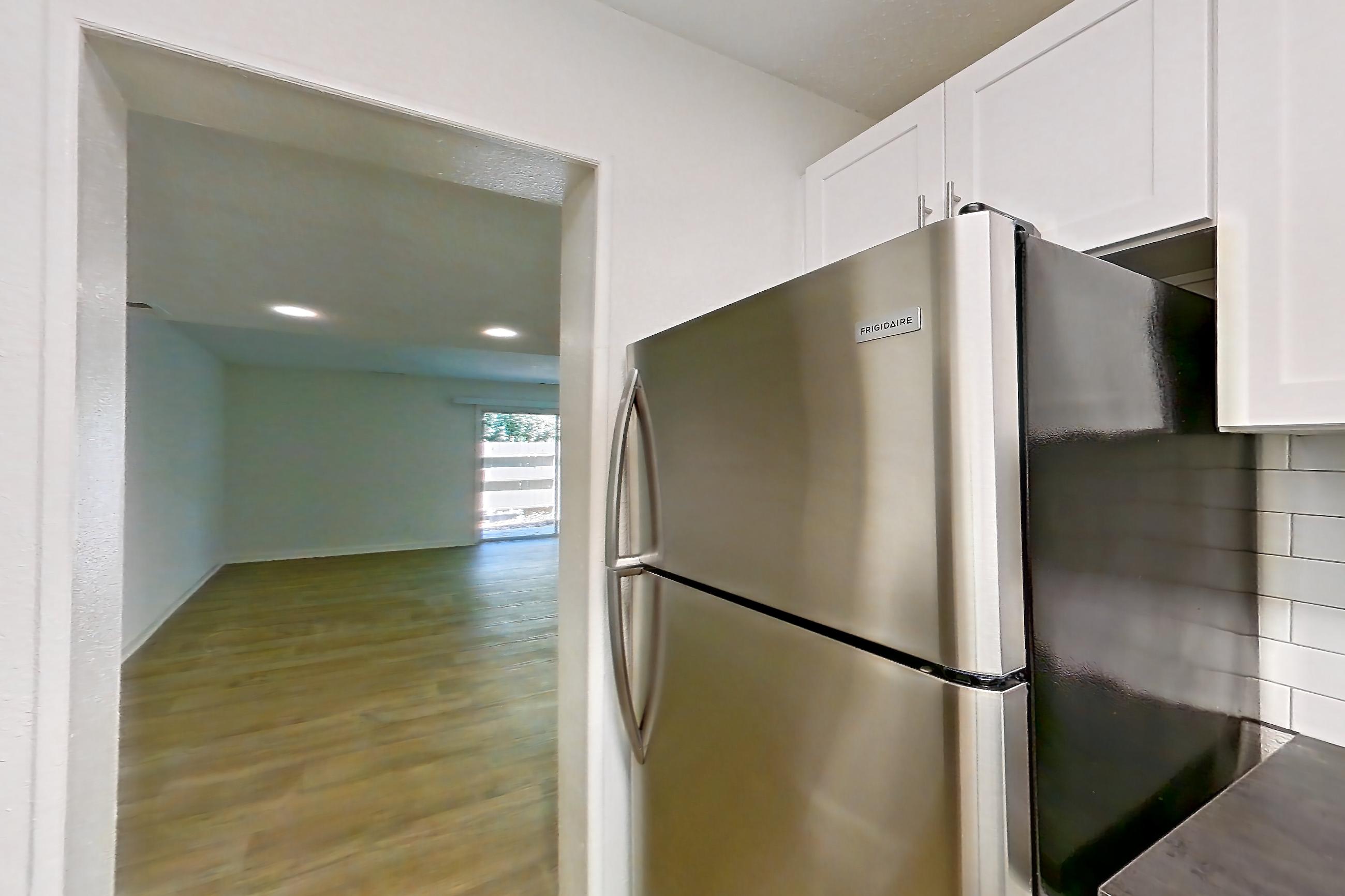 Kitchen with black appliances, dark countertops, dishwasher, electric range, light countertops, light wood-finish flooring, oven/range, range hood, refrigerator, and stainless steel appliances, Apartment L1452T at The Legacy at Druid Hills