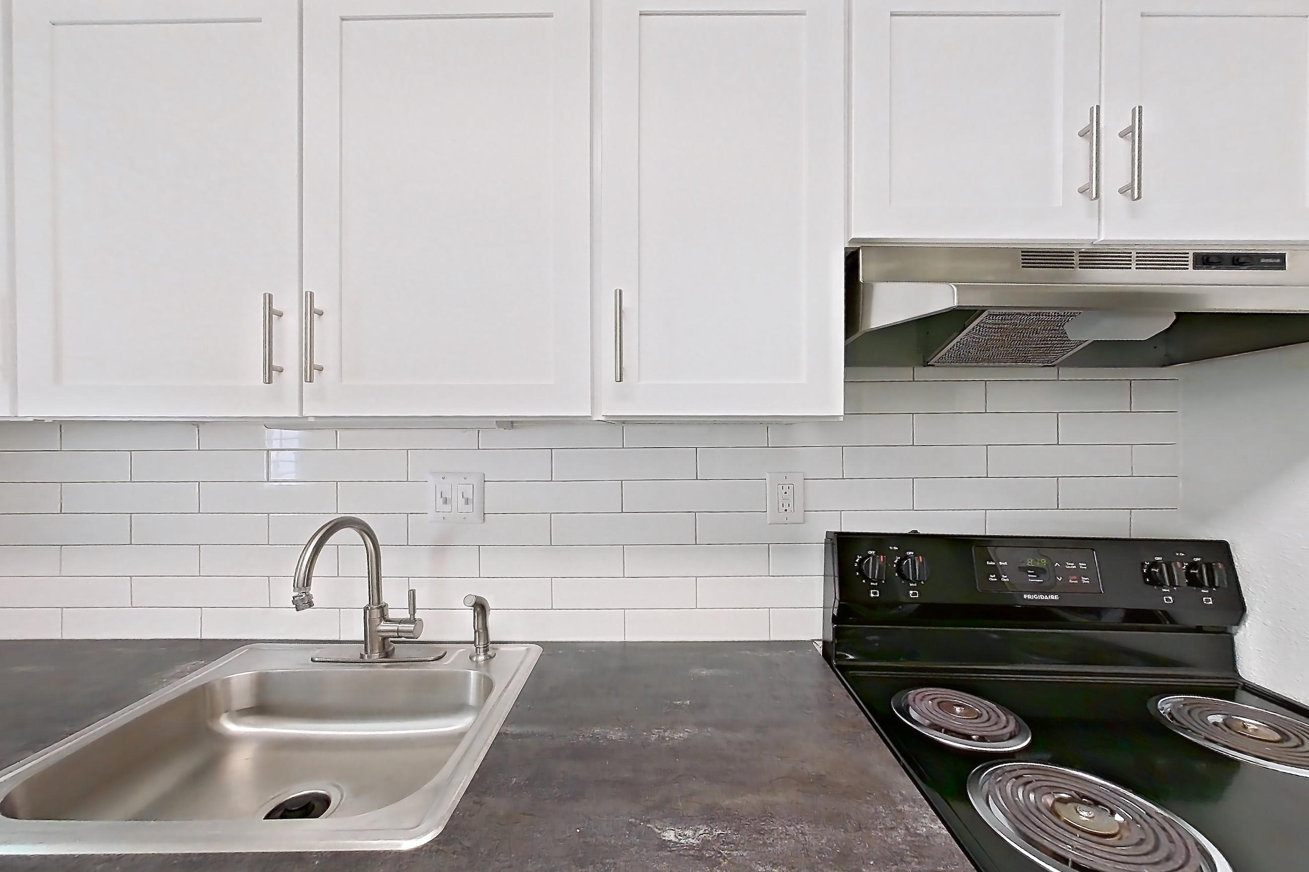 Kitchen with black appliances, dark countertops, dishwasher, electric range, light countertops, light wood-finish flooring, oven/range, range hood, refrigerator, and stainless steel appliances, Apartment L1452T at The Legacy at Druid Hills