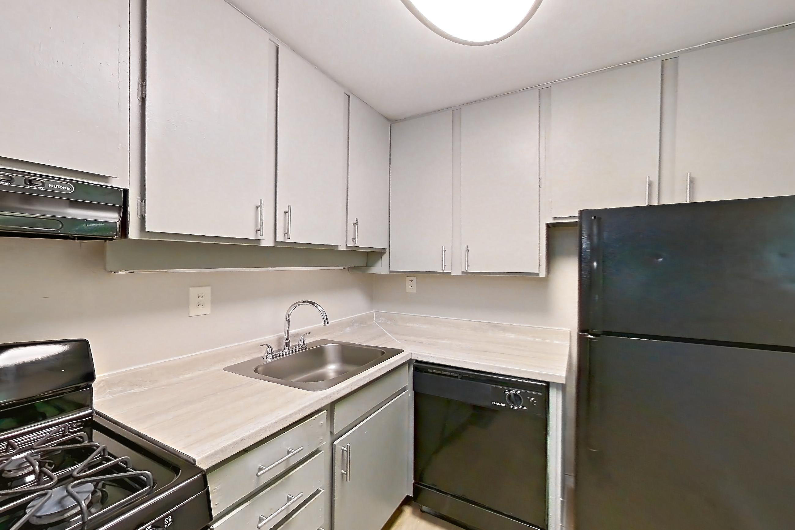 Kitchen with black appliances, dishwasher, gas range, light countertops, light wood-finish flooring, oven/range, range hood, and refrigerator, Apartment L1470A at The Legacy at Druid Hills