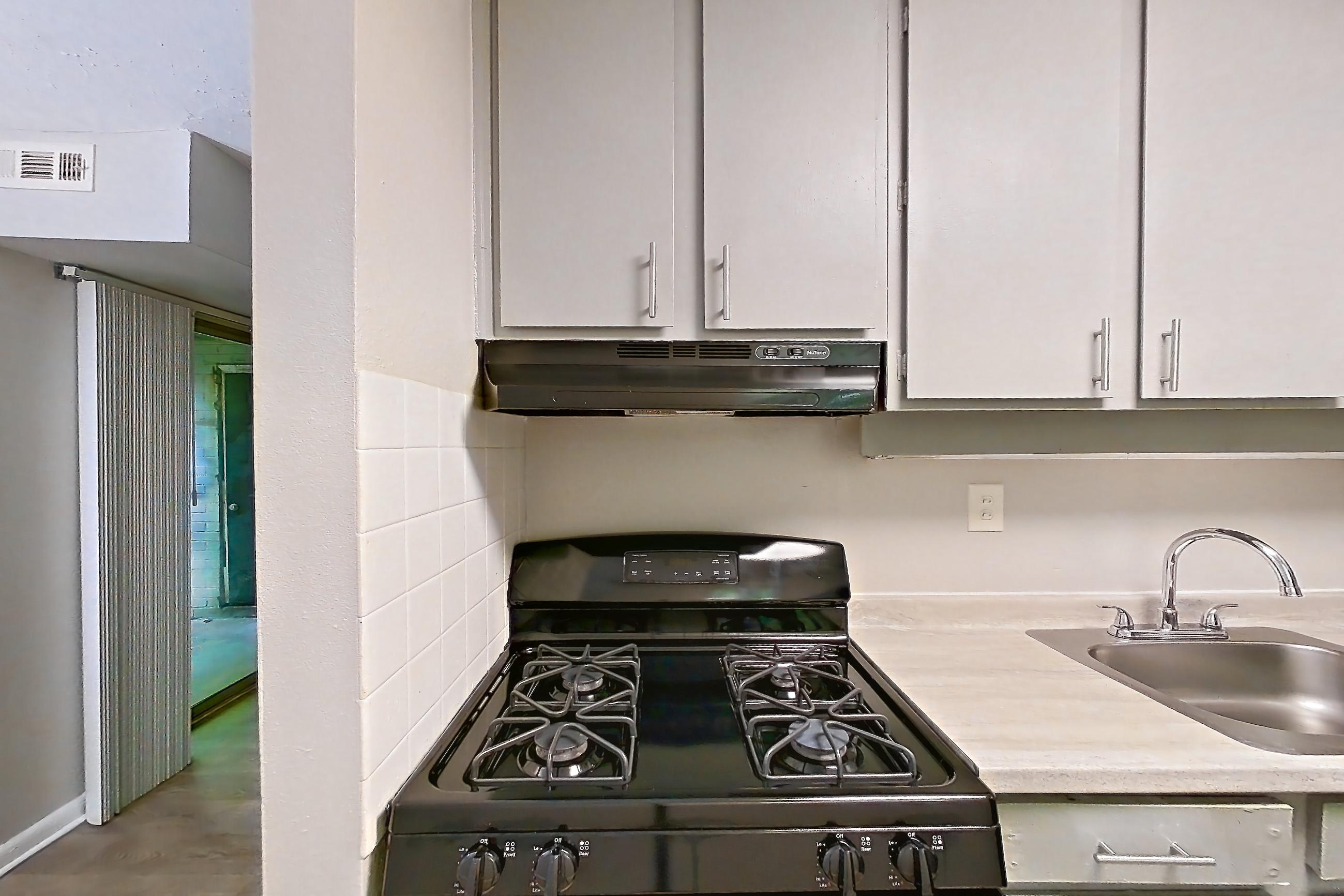 Kitchen with black appliances, dishwasher, gas range, light countertops, light wood-finish flooring, oven/range, range hood, and refrigerator, Apartment L1470A at The Legacy at Druid Hills