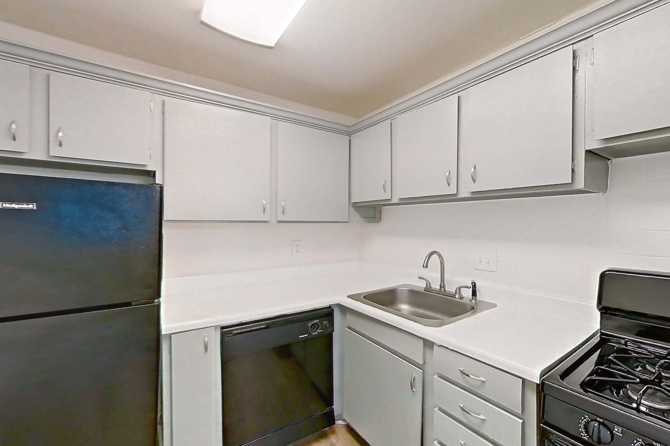 Kitchen with black appliances, dishwasher, gas range, light countertops, light wood-finish flooring, oven/range, and refrigerator, Apartment L1471F at The Legacy at Druid Hills