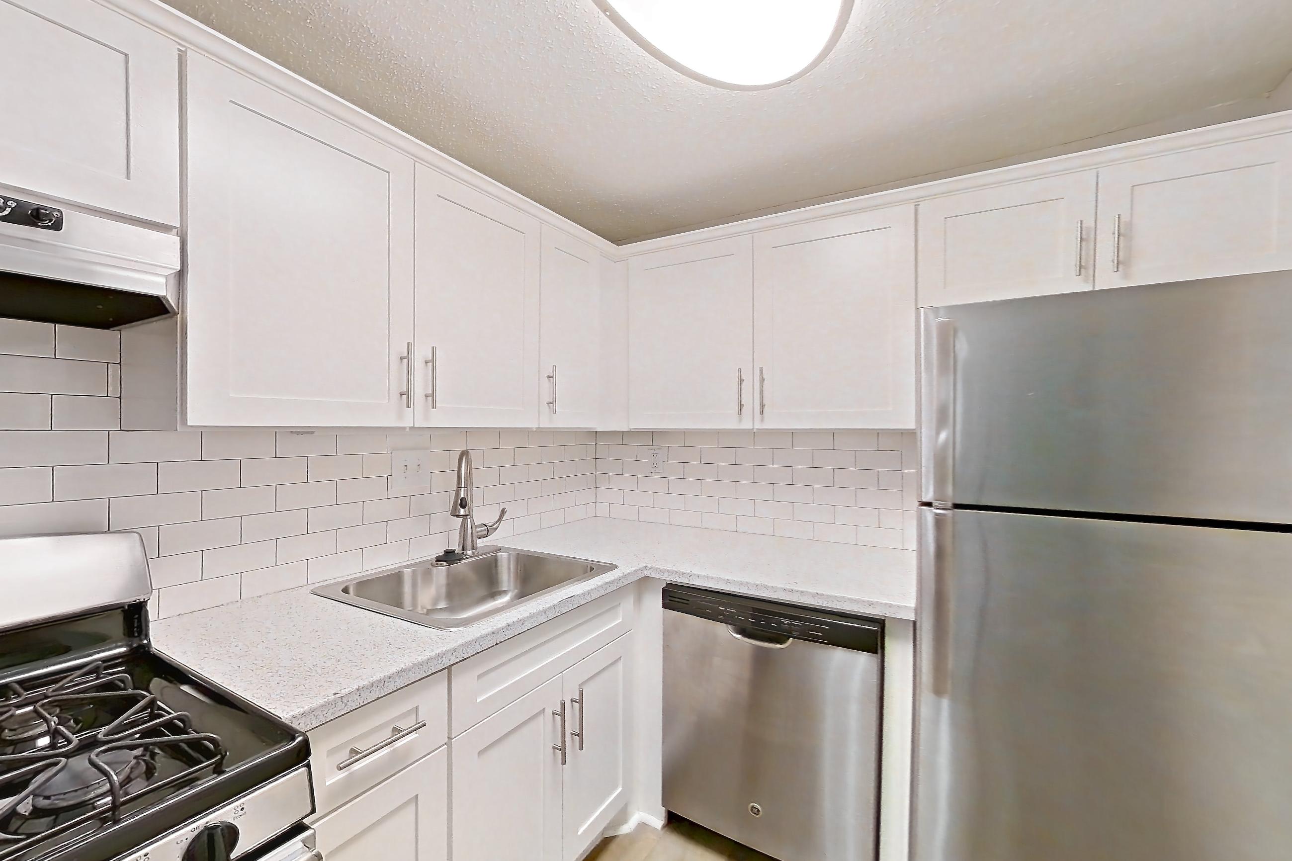 Kitchen with dark wood-finish flooring, dishwasher, gas range, light countertops, light stone countertops, light wood-finish flooring, oven/range, range hood, refrigerator, and stainless steel appliances, Apartment L1486C at The Legacy at Druid Hills