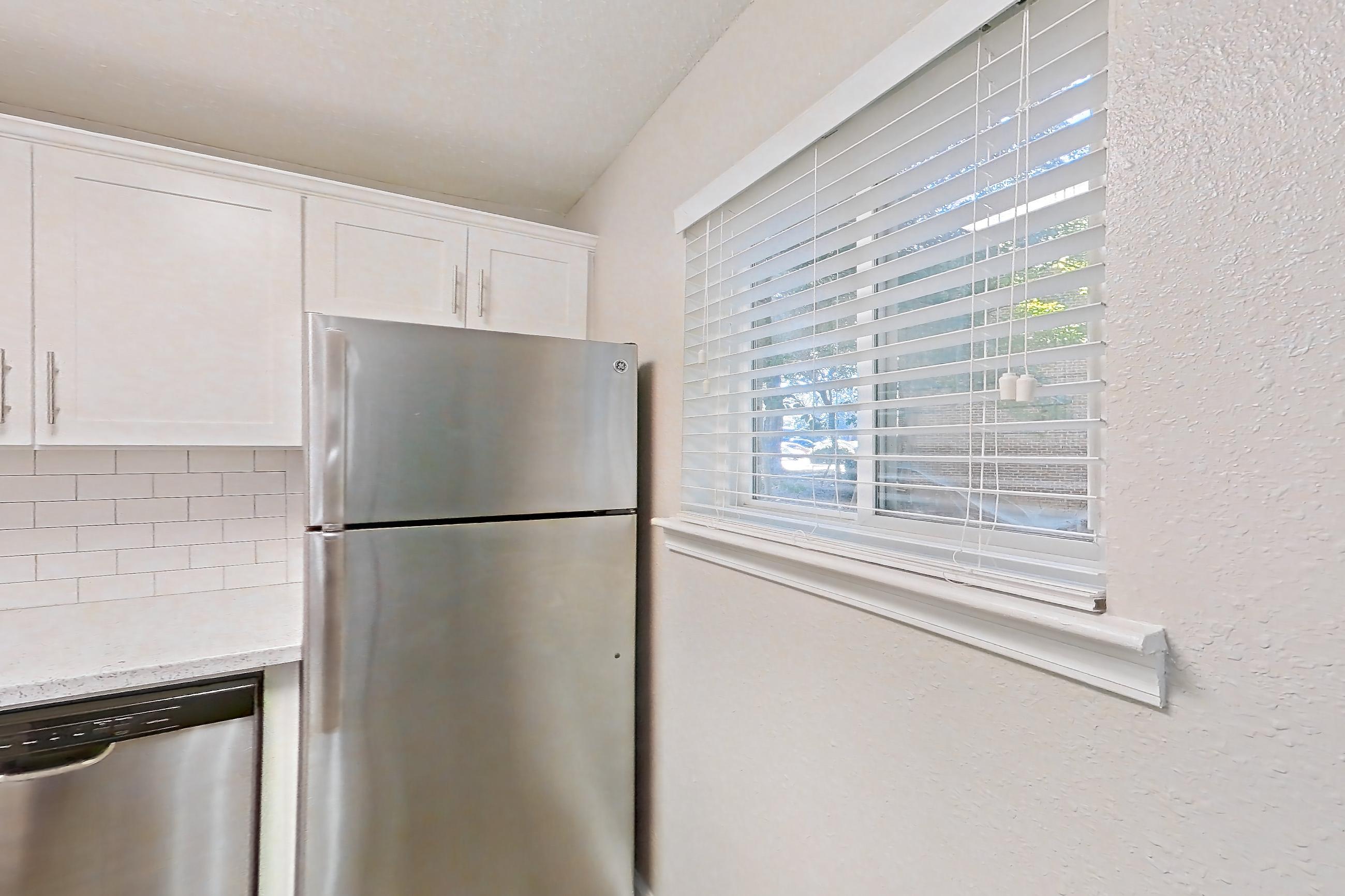 Kitchen with dark wood-finish flooring, dishwasher, gas range, light countertops, light stone countertops, light wood-finish flooring, oven/range, range hood, refrigerator, and stainless steel appliances, Apartment L1486C at The Legacy at Druid Hills