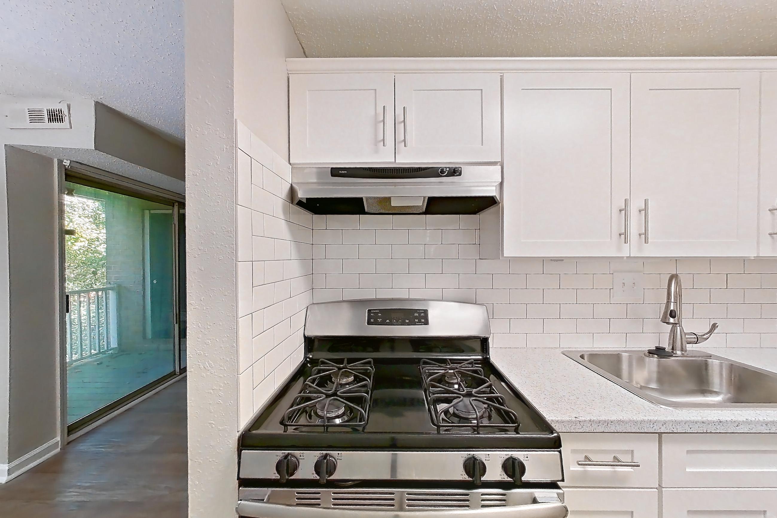 Kitchen with dark wood-finish flooring, dishwasher, gas range, light countertops, light stone countertops, light wood-finish flooring, oven/range, range hood, refrigerator, and stainless steel appliances, Apartment L1486C at The Legacy at Druid Hills