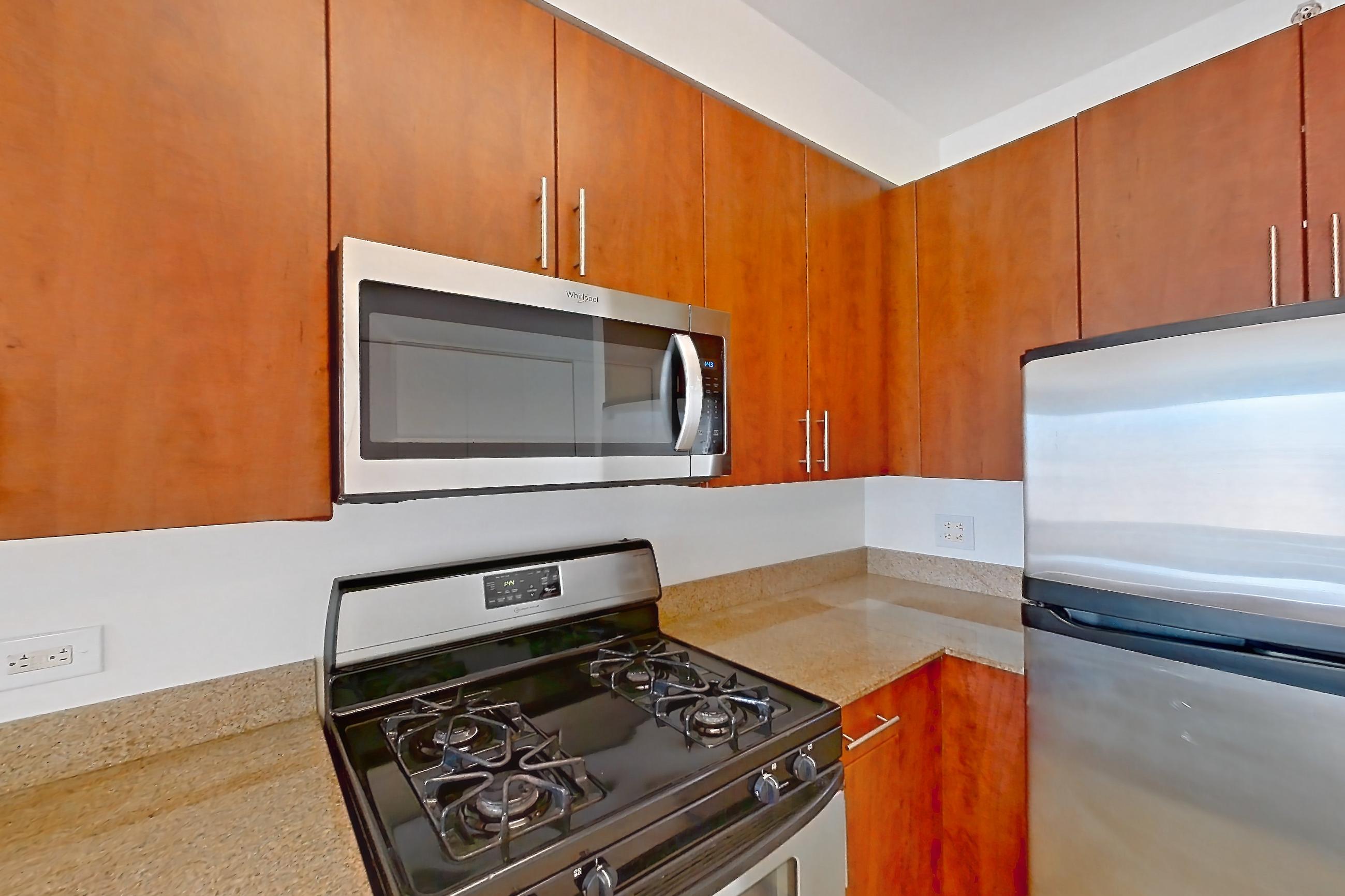 Kitchen with dishwasher, gas range, light countertops, light stone countertops, light tile flooring, light wood-finish flooring, microwave, oven/range, refrigerator, and stainless steel appliances, Apartment 1223 at The Octagon