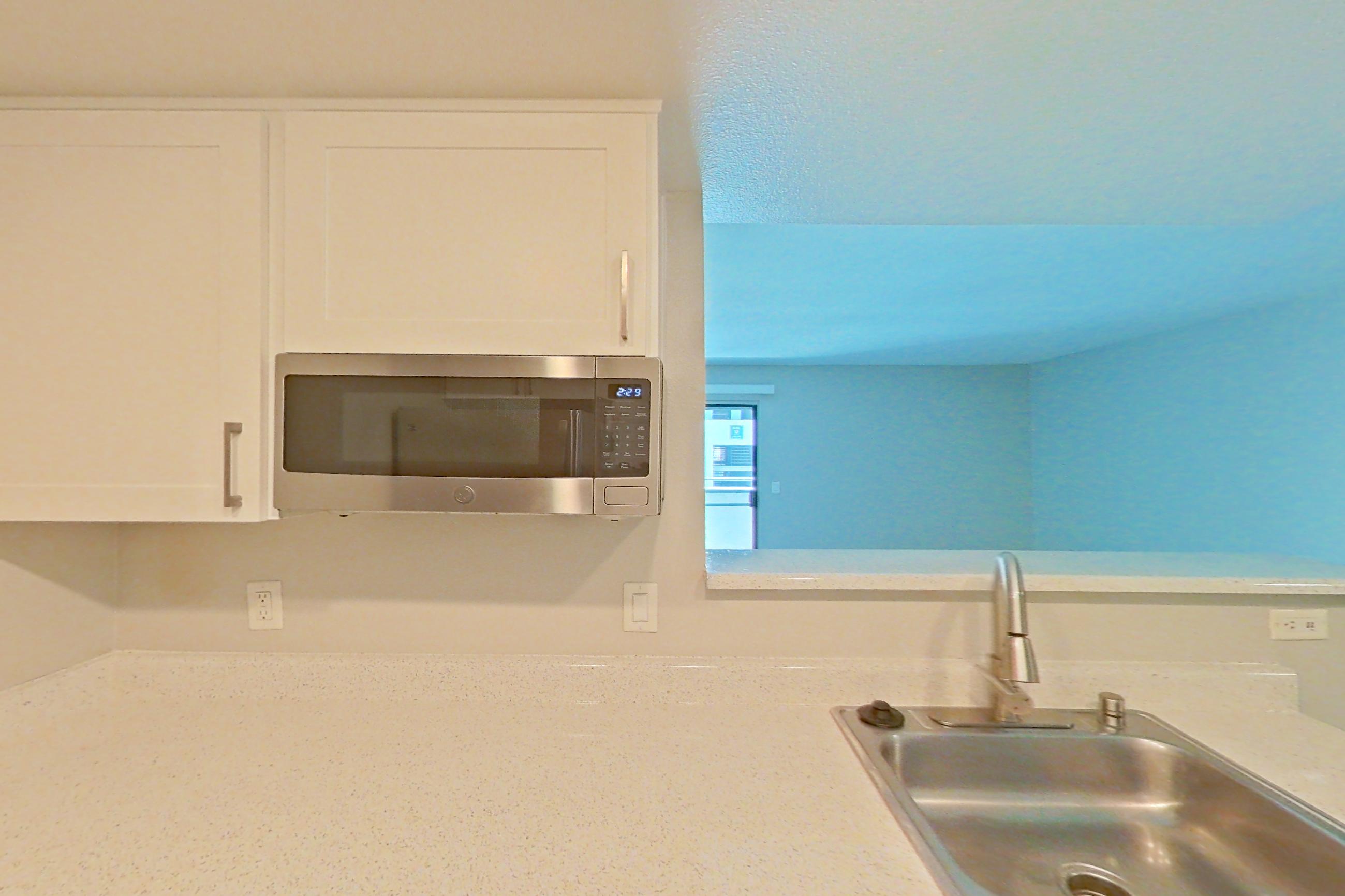 Kitchen with dishwasher, electric range, light countertops, light stone countertops, light wood-finish flooring, microwave, oven/range, refrigerator, and stainless steel appliances, Apartment 20 at Avana Rancho Cucamonga