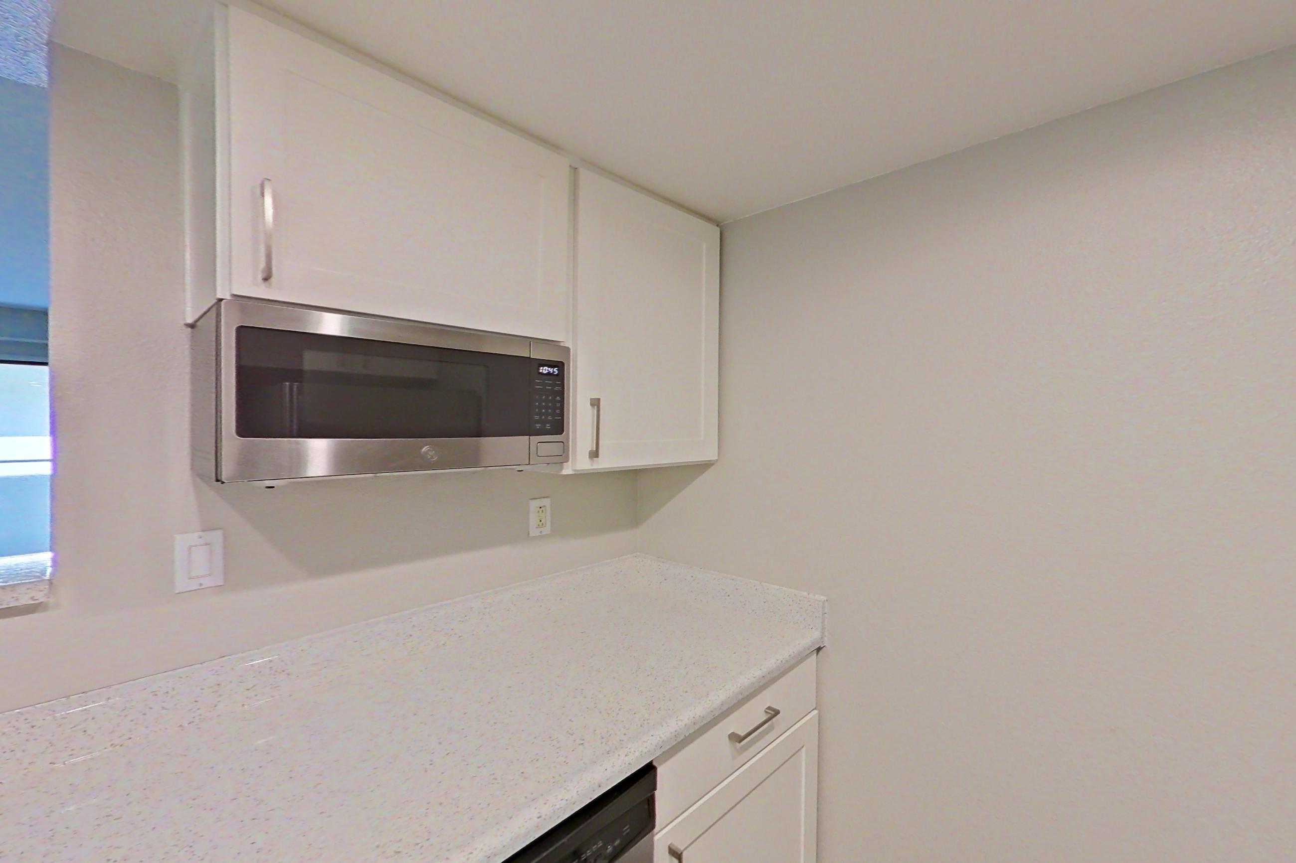 Kitchen with dishwasher, electric range, light stone countertops, light wood-finish flooring, microwave, oven/range, range hood, refrigerator, and stainless steel appliances, Apartment 18 at Avana Rancho Cucamonga