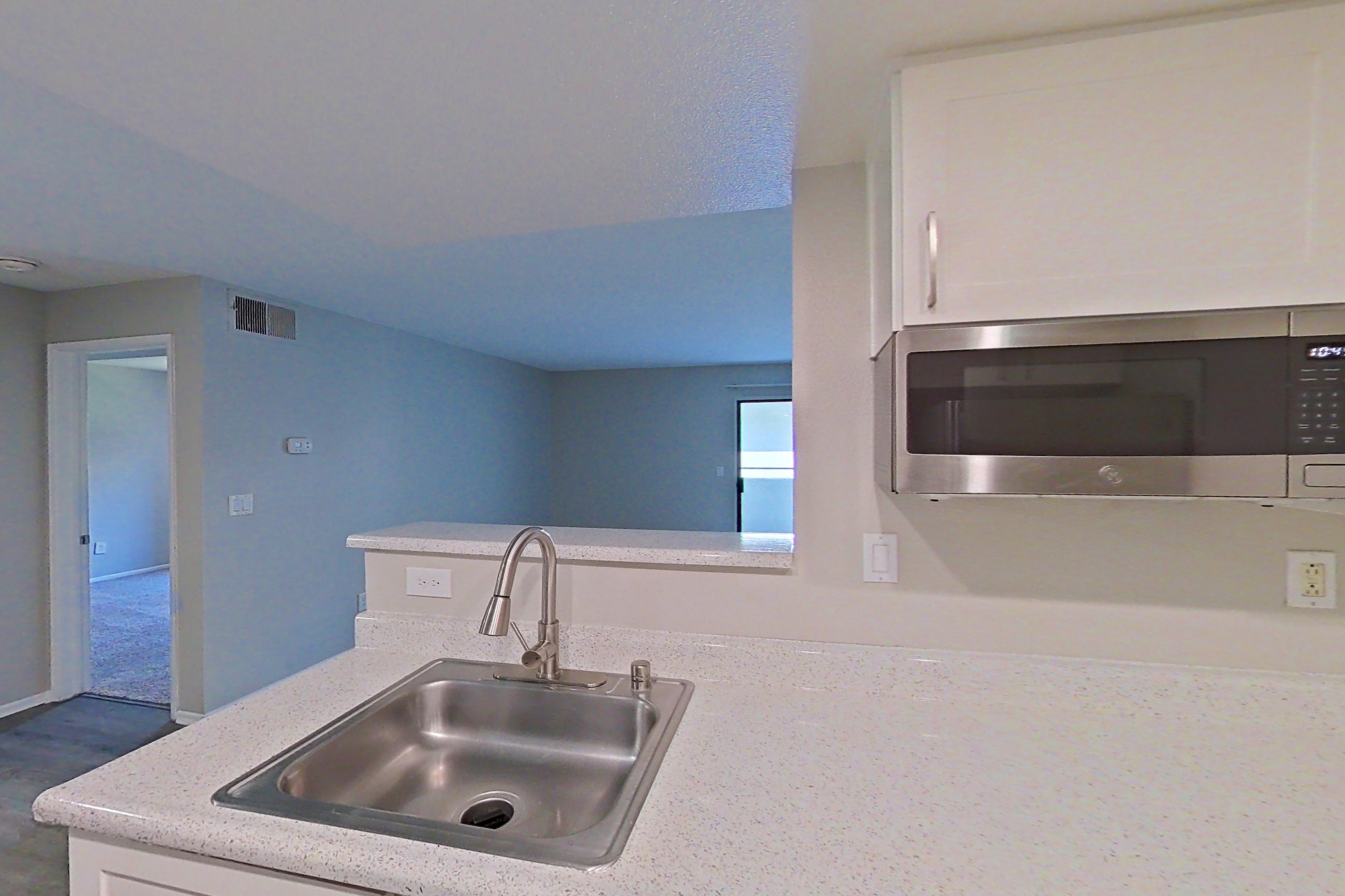 Kitchen with dishwasher, electric range, light stone countertops, light wood-finish flooring, microwave, oven/range, range hood, refrigerator, and stainless steel appliances, Apartment 18 at Avana Rancho Cucamonga