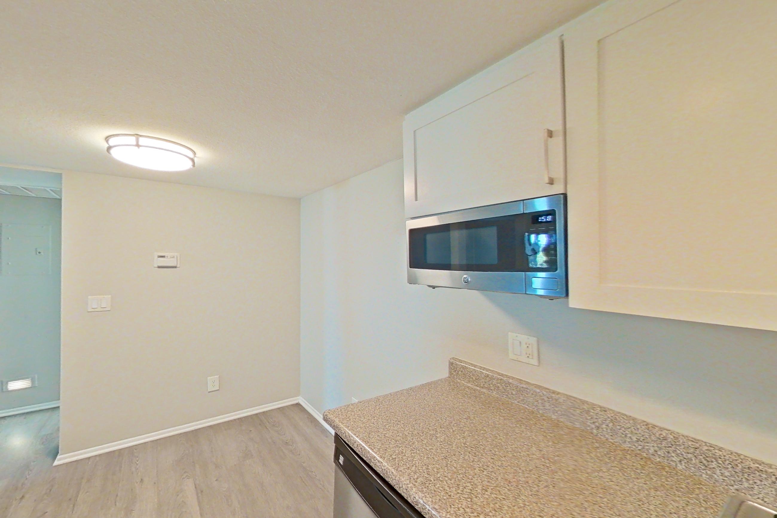 Kitchen with black appliances, dishwasher, electric range, light stone countertops, light wood-finish flooring, microwave, oven/range, range hood, and stainless steel appliances, Apartment 02 at Avana Rancho Cucamonga