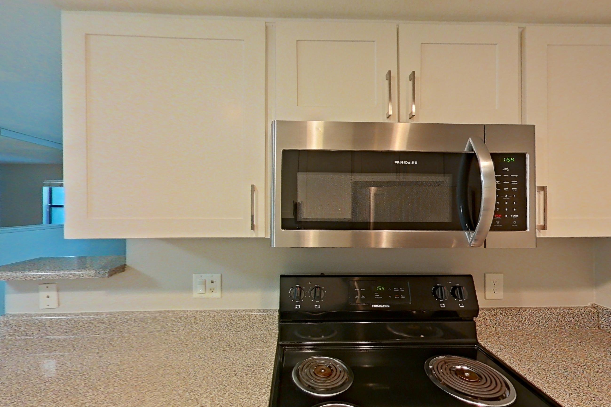 Kitchen with black appliances, dishwasher, electric range, light countertops, light stone countertops, light wood-finish flooring, microwave, oven/range, refrigerator, and stainless steel appliances, Apartment 06 at Avana Rancho Cucamonga